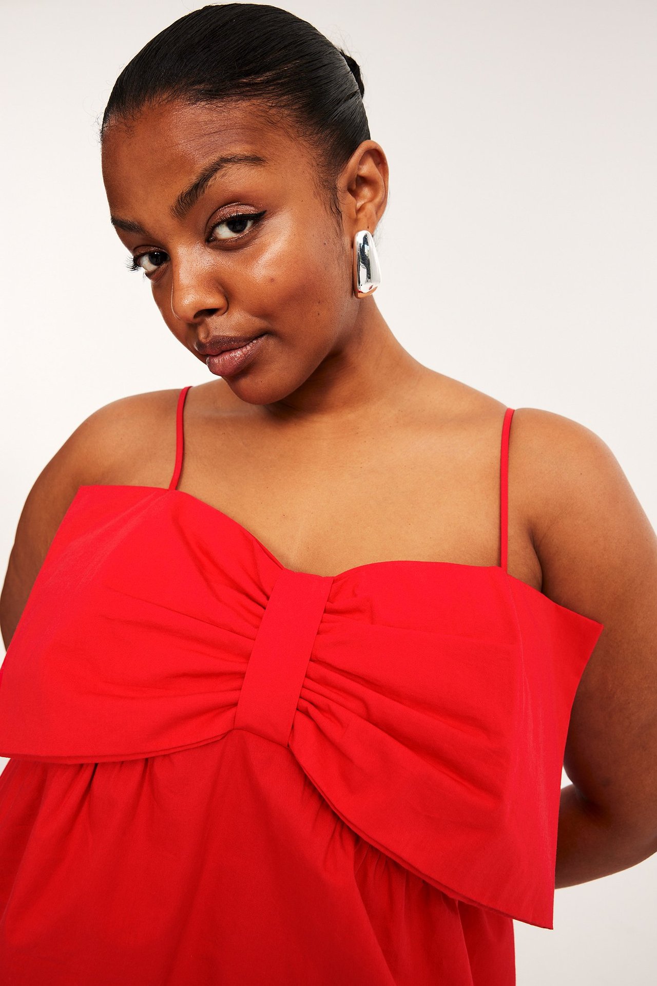 Nærbilde forfra av en kvinne i rød peplumtopp med stor sløyfe og sølvfargede øreringer.