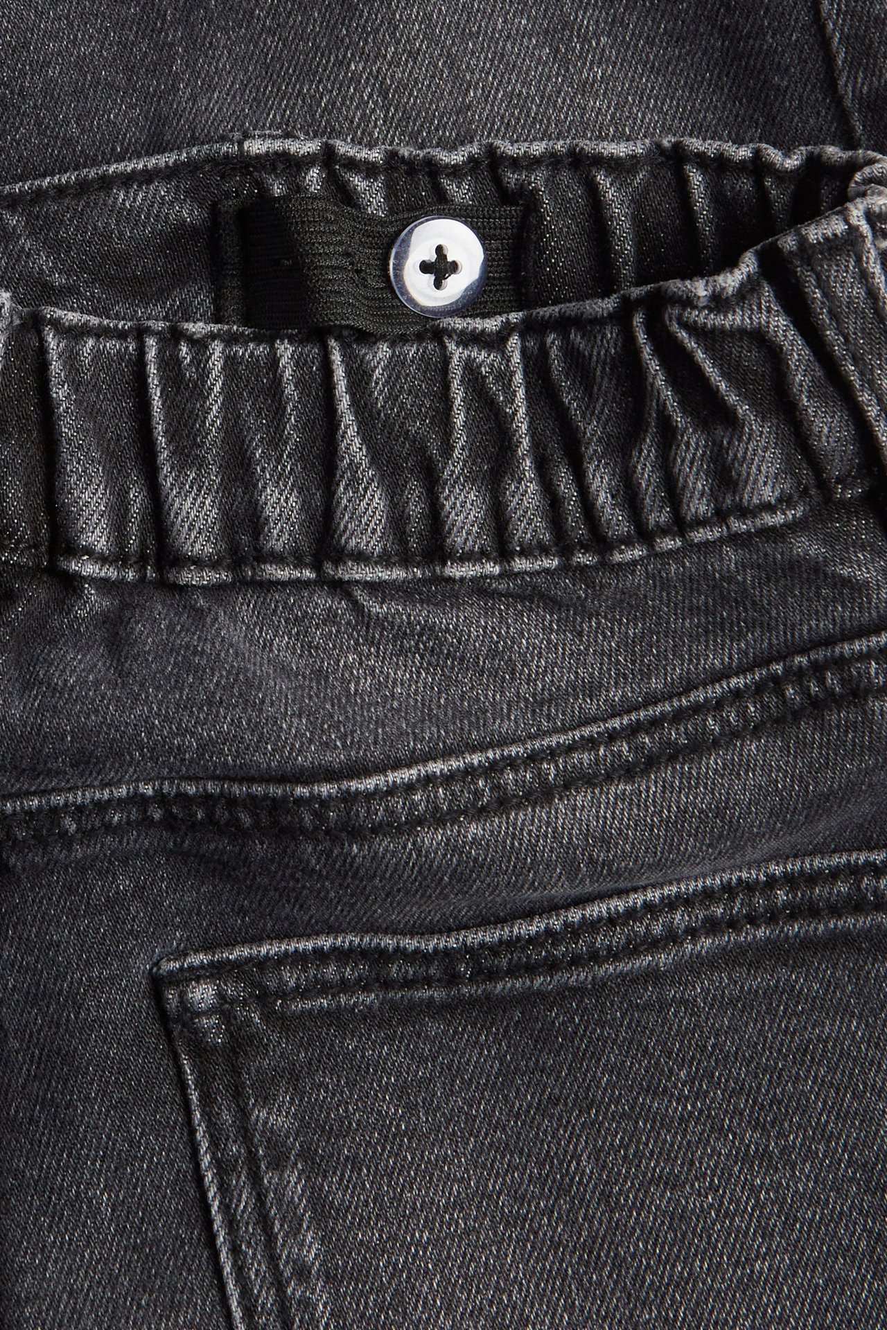 Zbliżenie szarych dżinsów relaxed z elastycznym, regulowanym pasem i białym guzikiem.