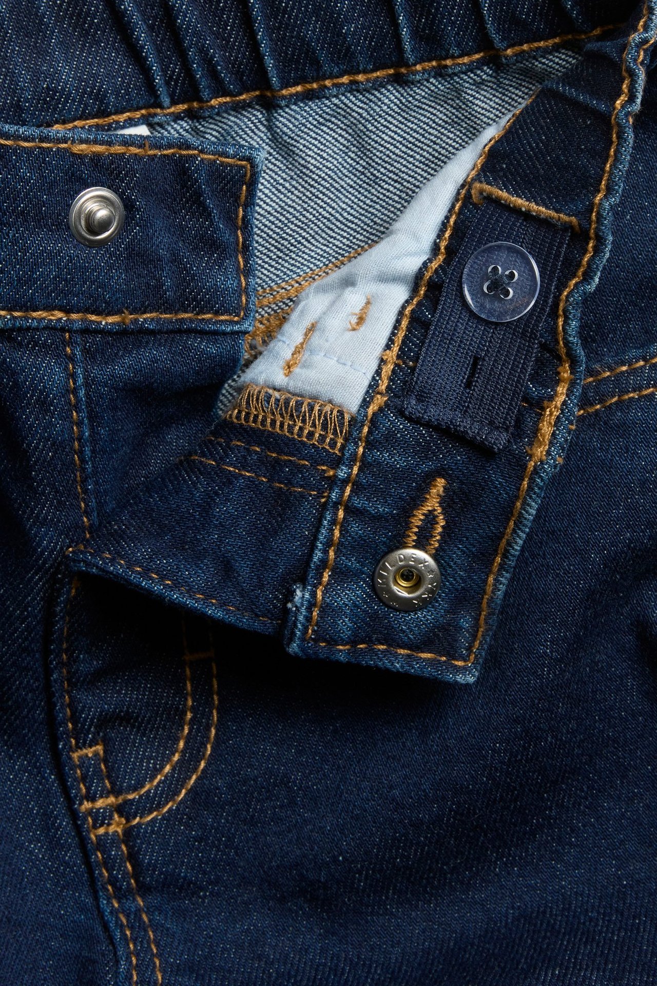 Zbliżenie na ciemnoniebieskie dżinsy dziecięce: elastyczna talia, zatrzask i regulowana wewnętrzna gumka.