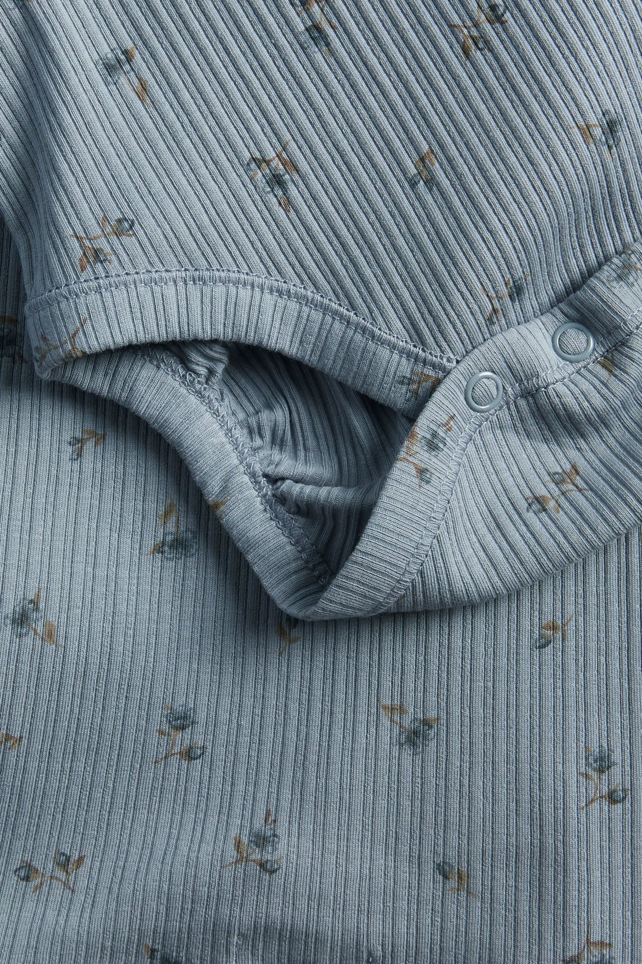 Lähikuva vaaleansinisestä ribatusta pitkähihaisesta vauvan body-paidasta kukkakuviolla ja neppareilla.