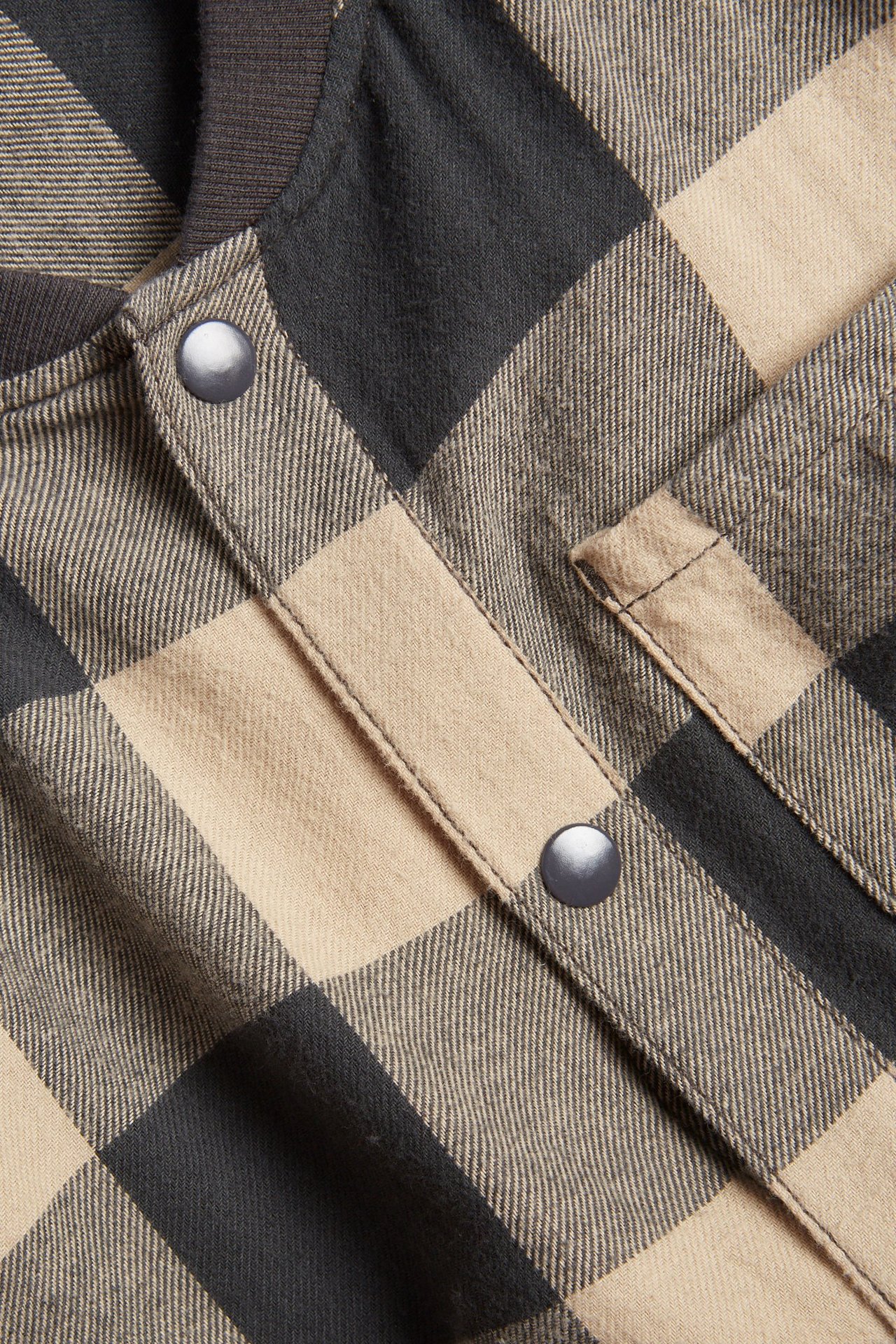 Zbliżenie beżowo-szarej koszuli flanelowej w kratę, z zatrzaskami i prążkowanym kołnierzem.