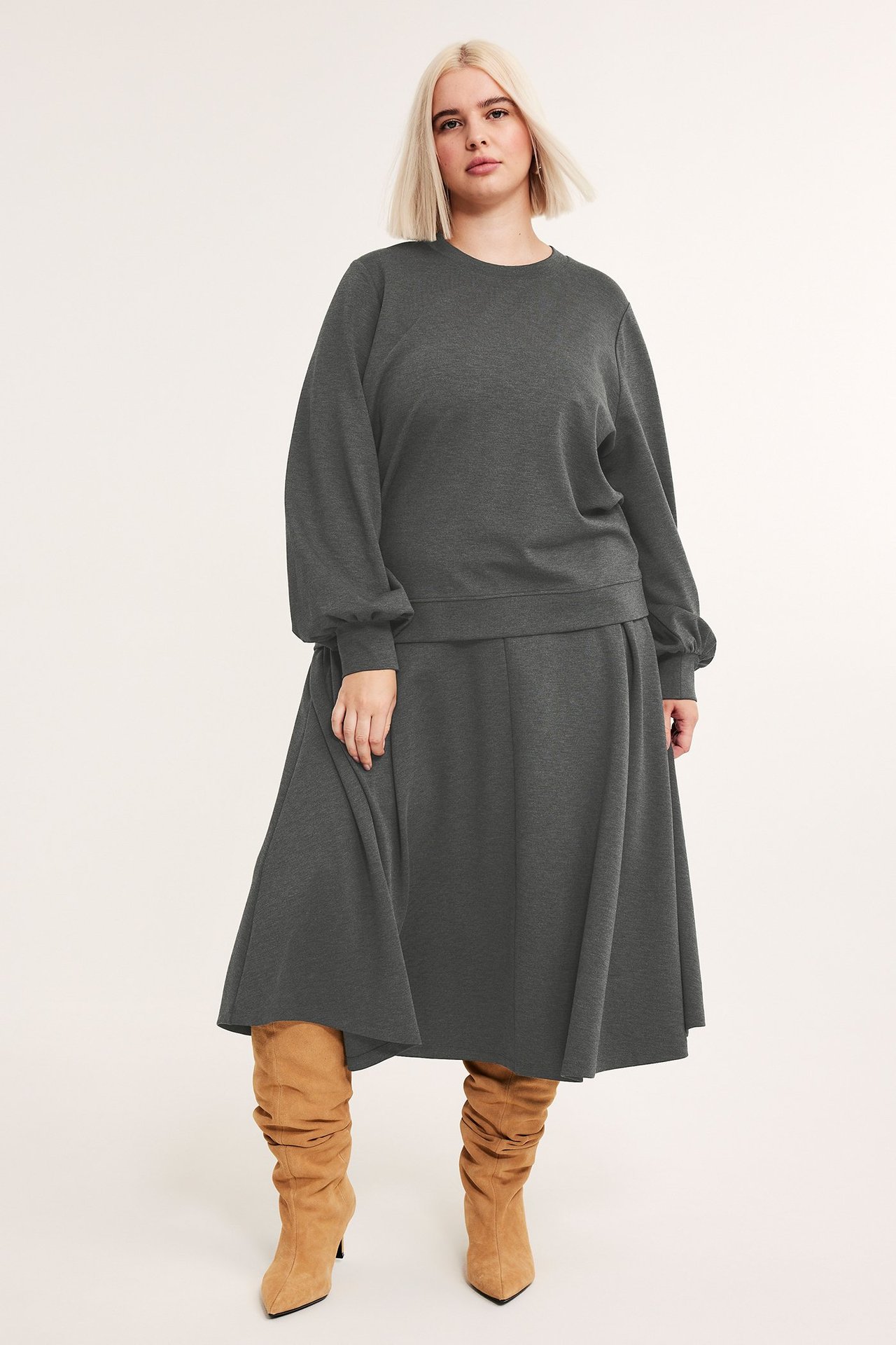 Frontvisning: Kvinne i mørkegrå melert sweatshirt med ballongermer, matchende midiskjørt og brune støvler.