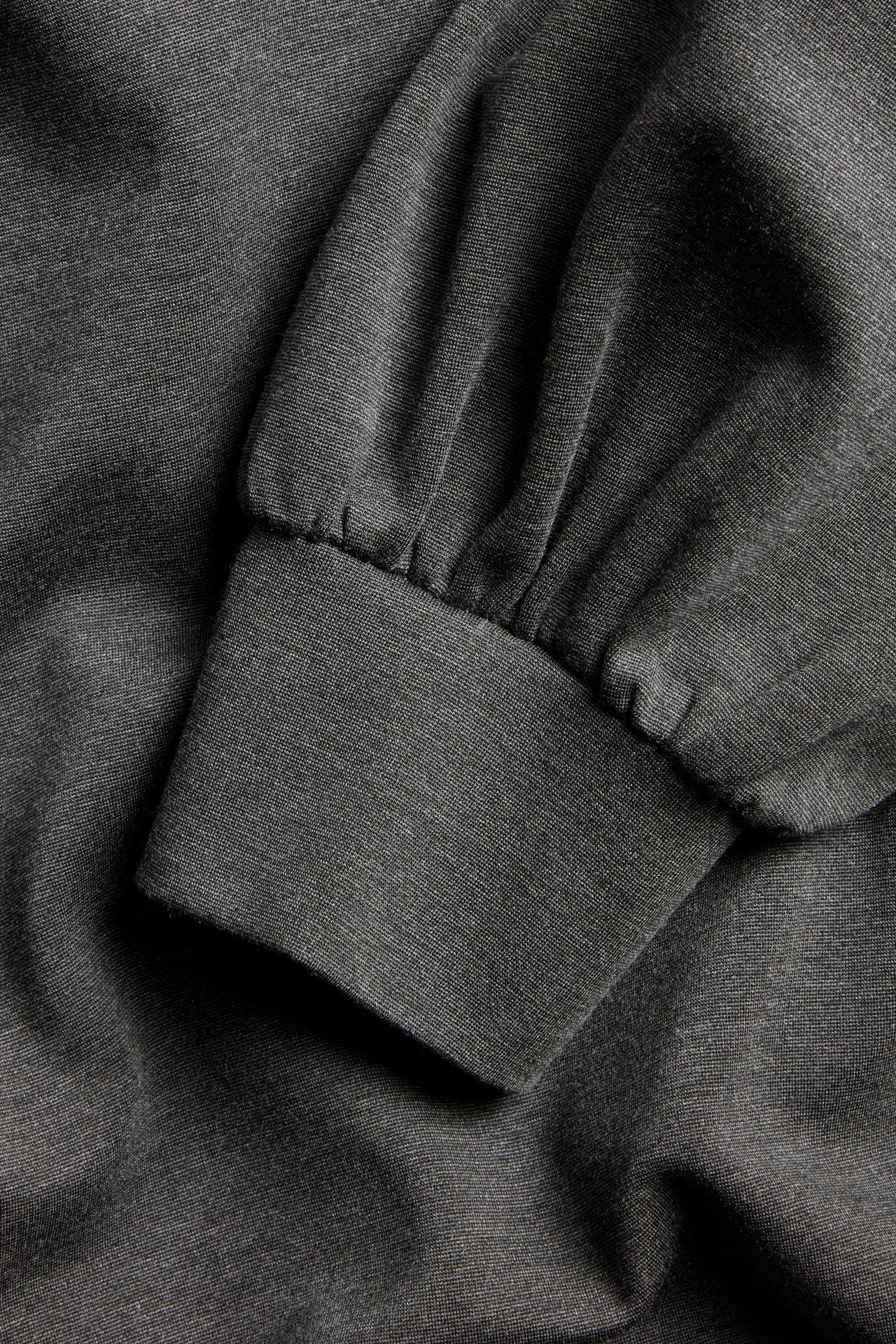 Zbliżenie na ciemnoszarą melanżową bluzę z bufiastym rękawem i prążkowanym mankietem.