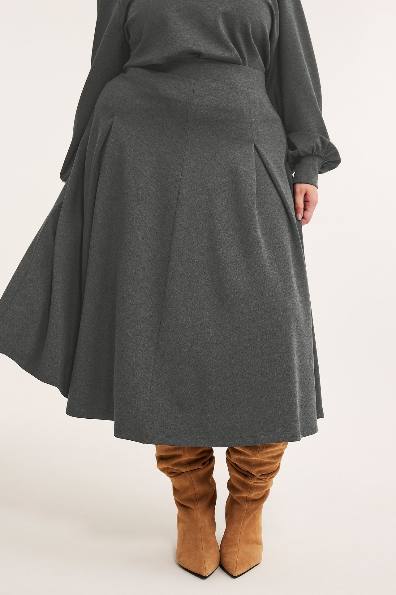 Edestä: nainen tummanharmaassa meleeratussa viskoosihameessa, yhteensopivassa topissa ja ruskeissa polvisaappaissa.