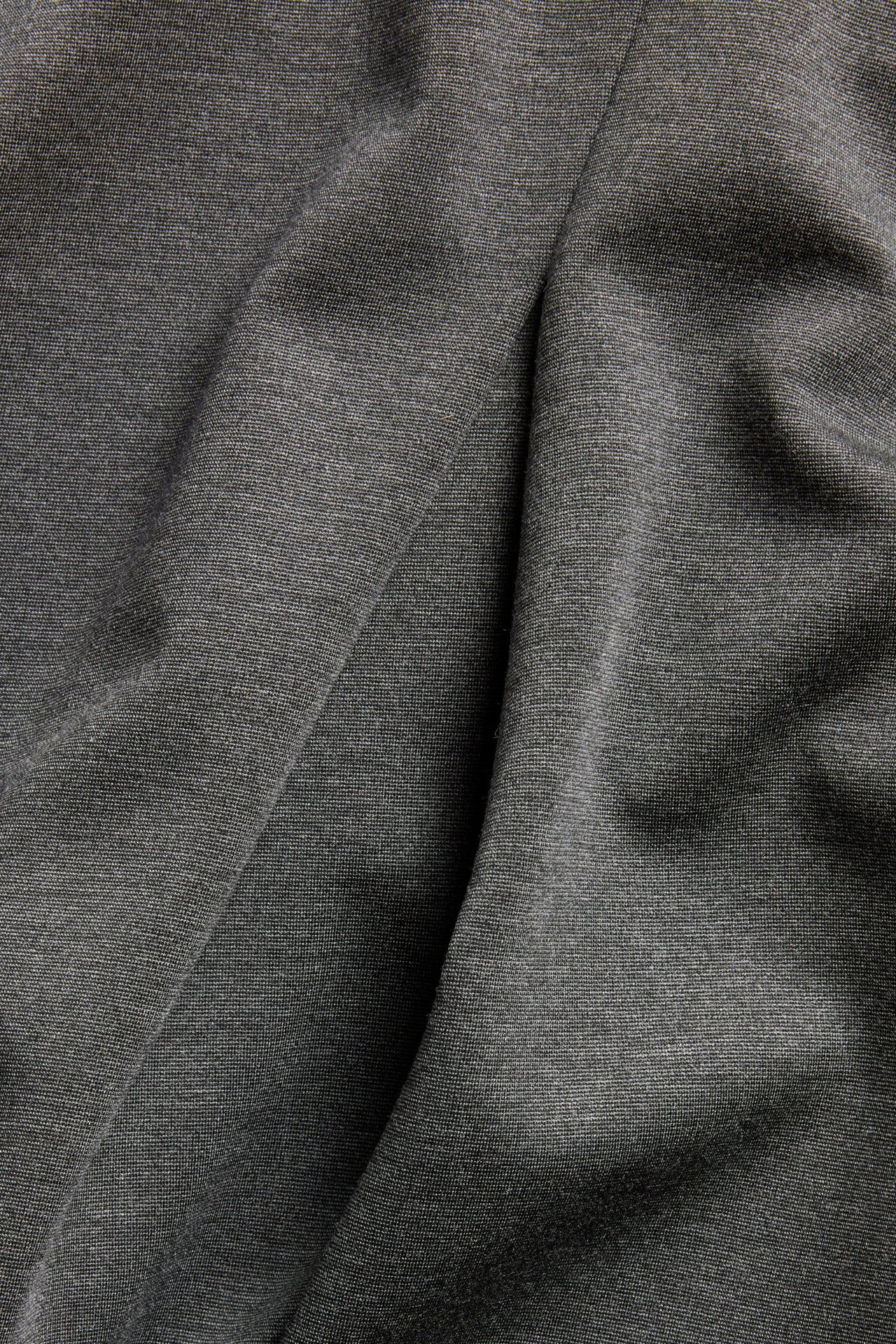 Zbliżenie na ciemnoszary melanżowy materiał rozkloszowanej spódnicy z miękkimi fałdami.