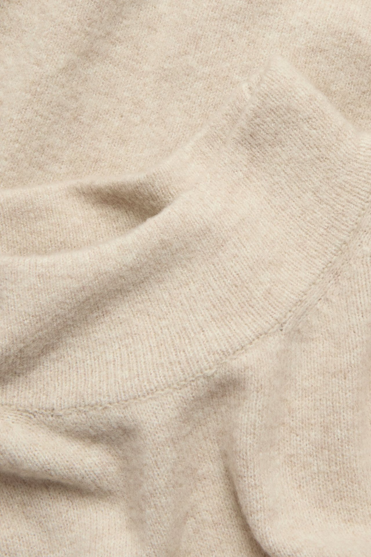 Zbliżenie beżowego melanżowego swetra z golfem o strukturalnym splocie.