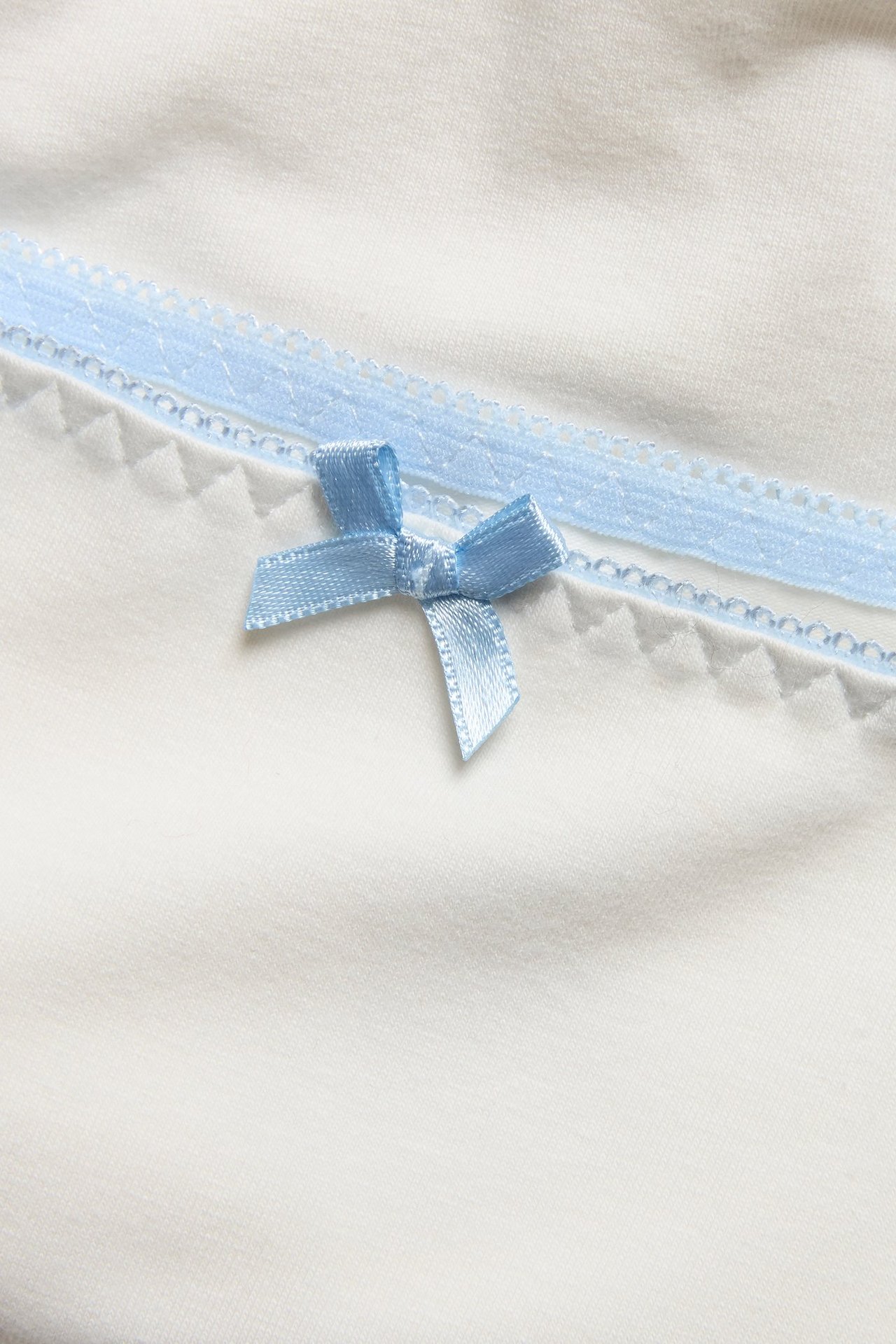 Zbliżenie białych bawełnianych bokserek z jasnoniebieską koronkową lamówką i małą niebieską kokardką.