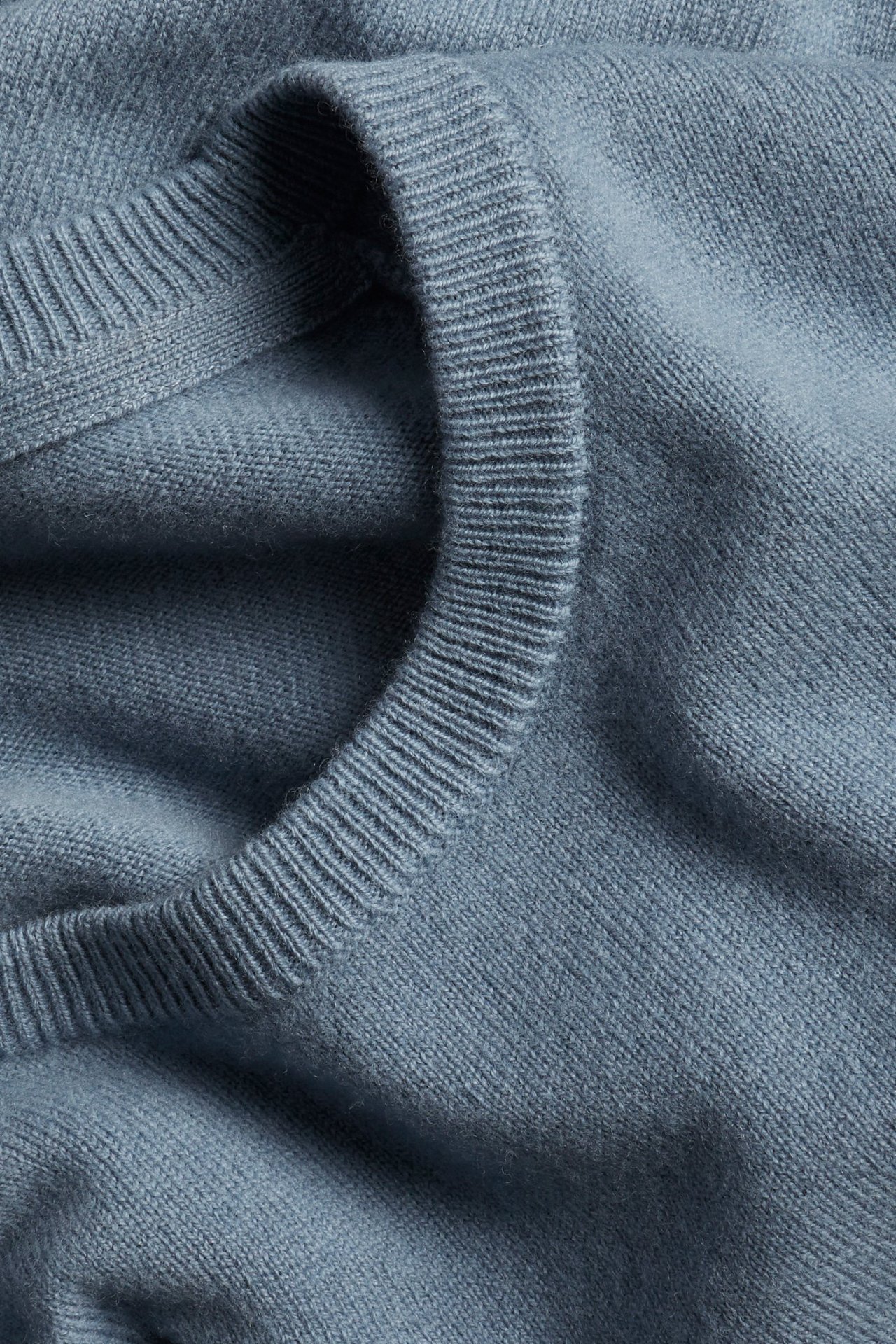 Zbliżenie niebieskiego, jednolitego swetra wełnianego z okrągłym dekoltem i ściągaczem.