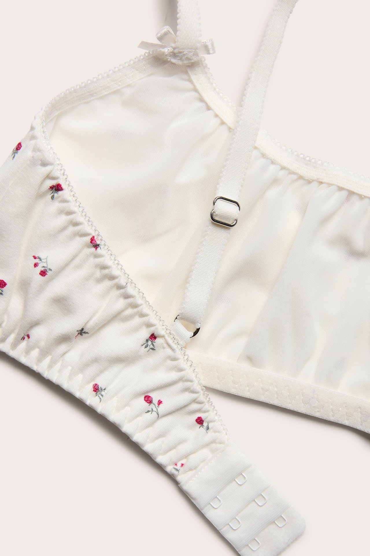 Zbliżenie na kremowy miękki biustonosz z drobnym czerwonym wzorem kwiatowym, regulowanymi ramiączkami i zapięciem z tyłu.