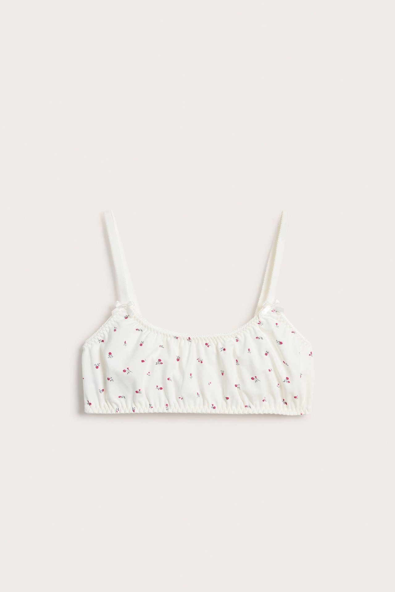 Framifrån: Offwhite mjuk bh med små röda blommönster, tunna justerbara axelband med rosetter, resårkant.