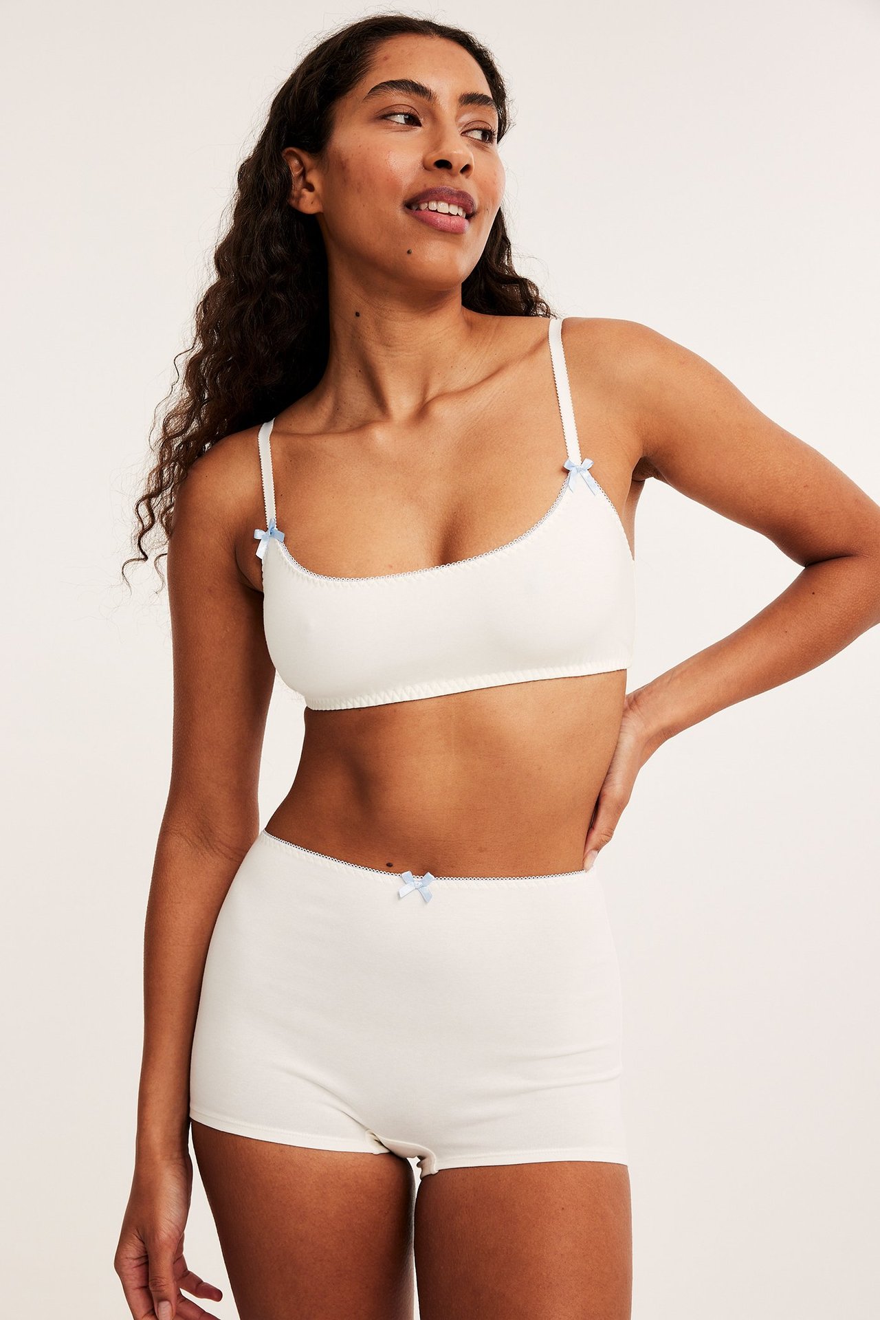 Framifrån, kvinna i vit mjuk-bh med ljusblå rosetter och matchande vita boxershorts.