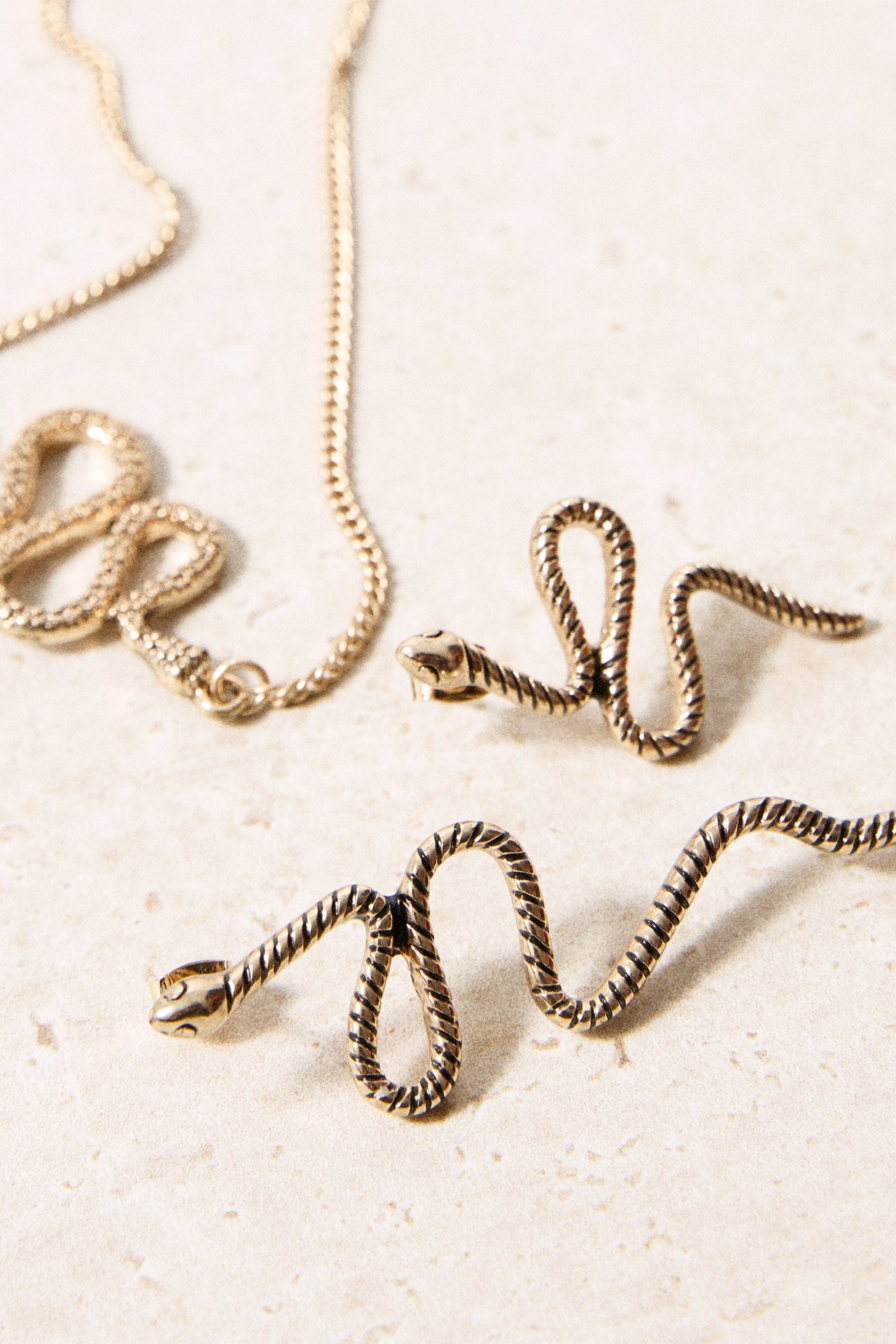 Zbliżenie dwóch złotych kolczyków w kształcie węża z metalu i łańcuszka.