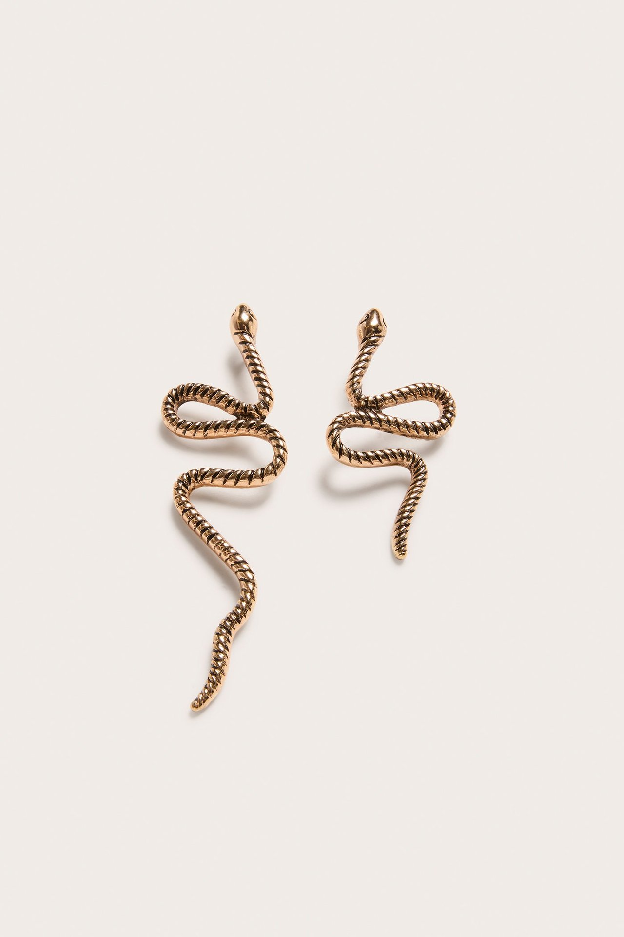 Zbliżenie dwóch złotych, metalowych kolczyków w kształcie węża z teksturowanymi korpusami.