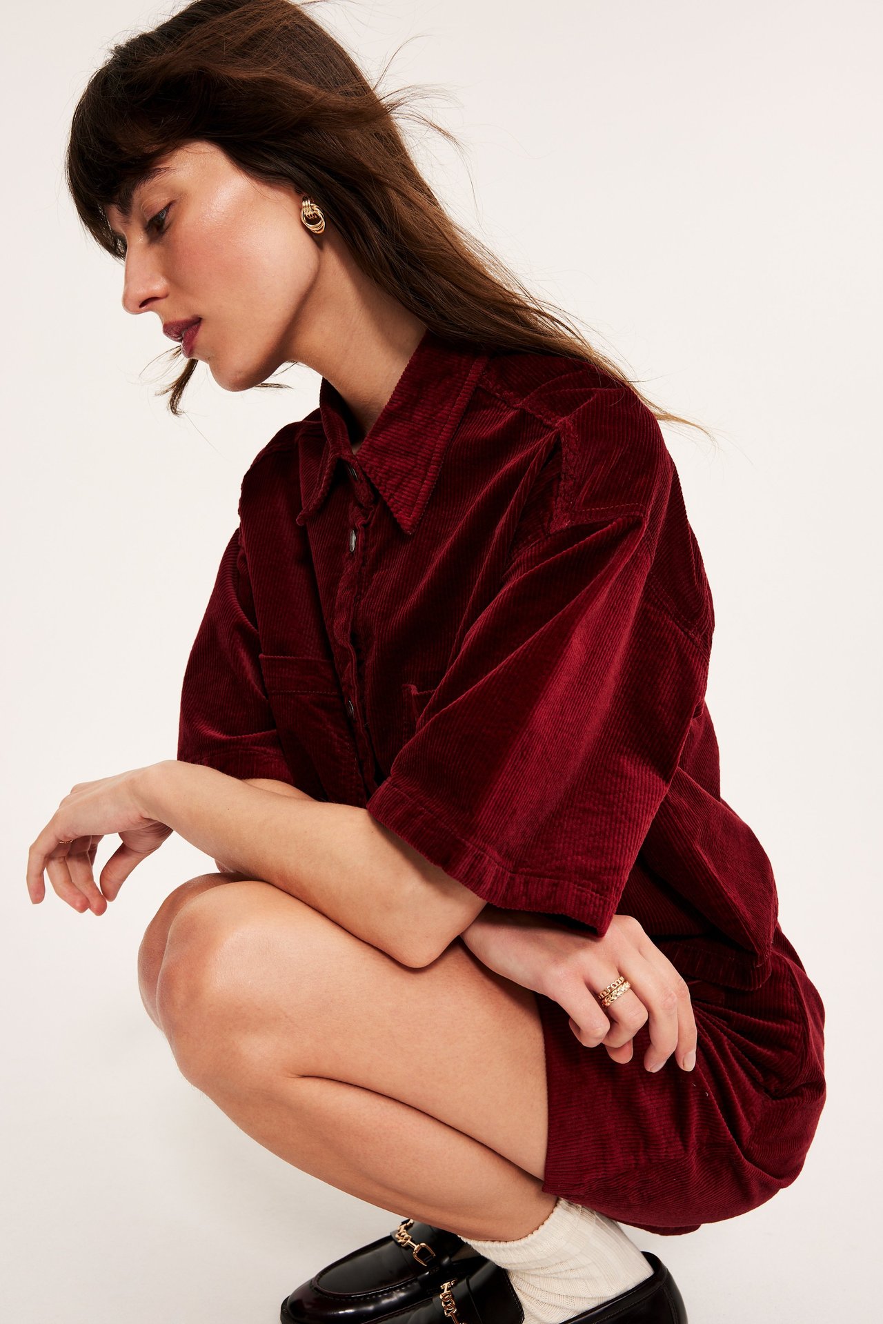 Kvinnes profilbilde i et rødt kort kordfløyelsskjørt, matchende skjorte, gulløredobber og sorte loafers.