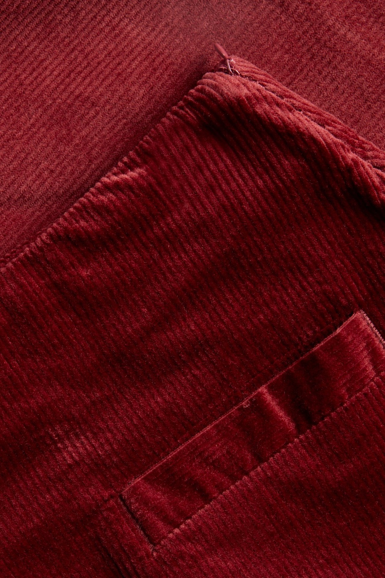 Zbliżenie czerwonej krótkiej spódnicy sztruksowej z widoczną kieszenią i bocznym zamkiem błyskawicznym.