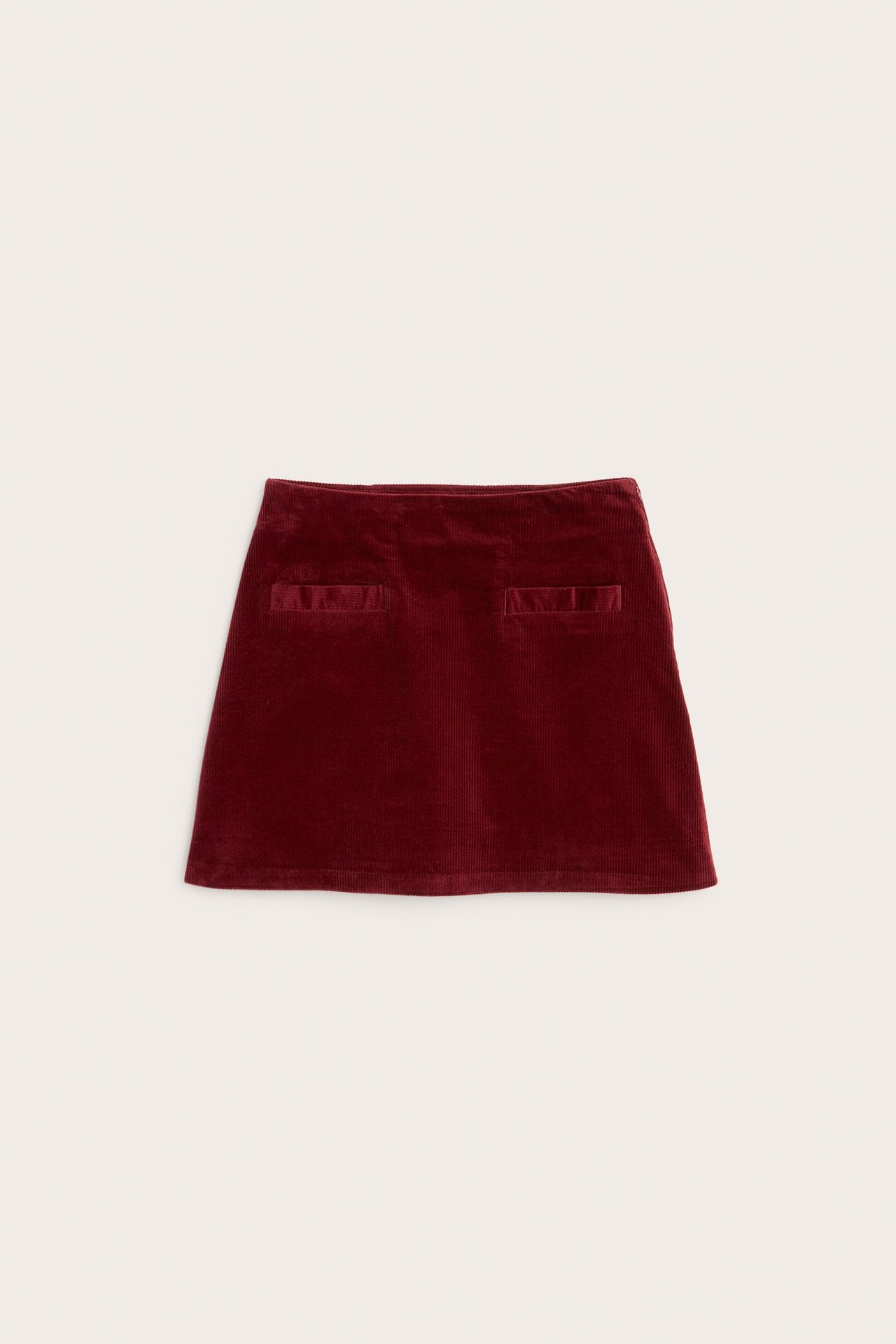 Frontvisning av et kort, rødt kordfløyelsskjørt med to rektangulære frontlommer.