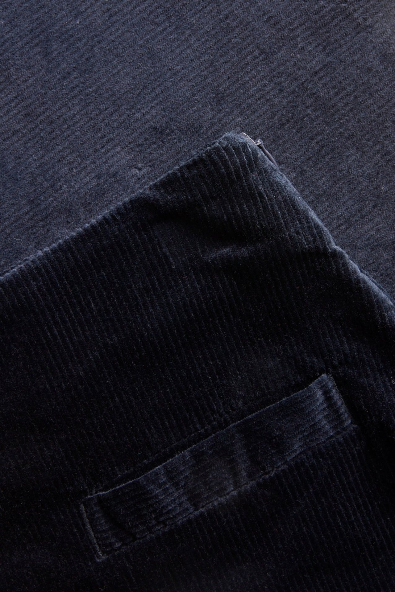 Zbliżenie na ciemnoniebieską sztruksową spódnicę, z kieszenią i bocznym zamkiem błyskawicznym.
