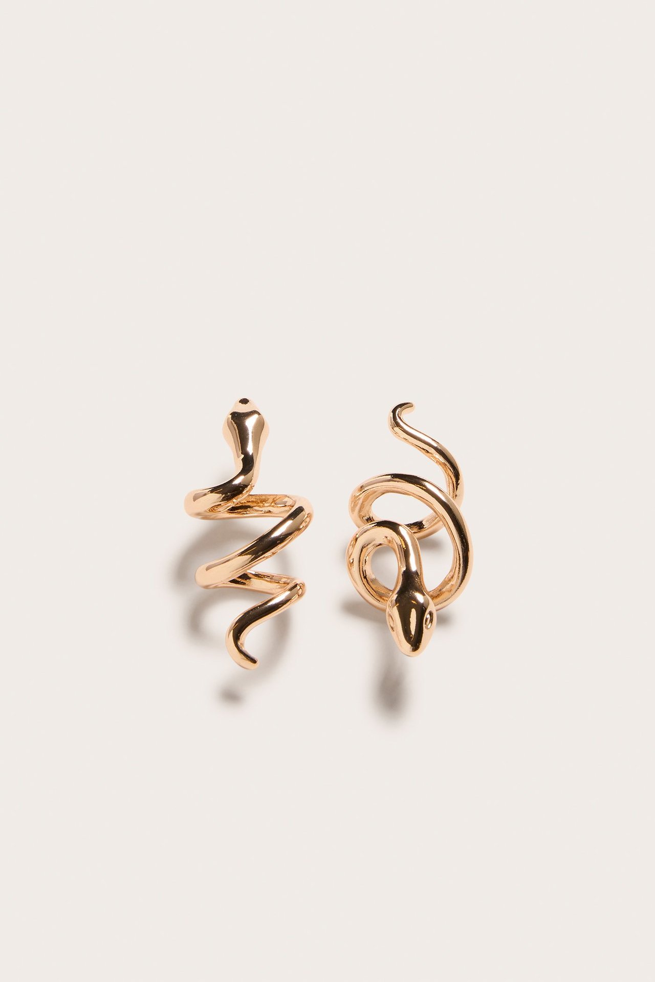 Närbild av två guldfärgade metallörhängen formade som ormar, var och en slingrad med synligt ormhuvud.