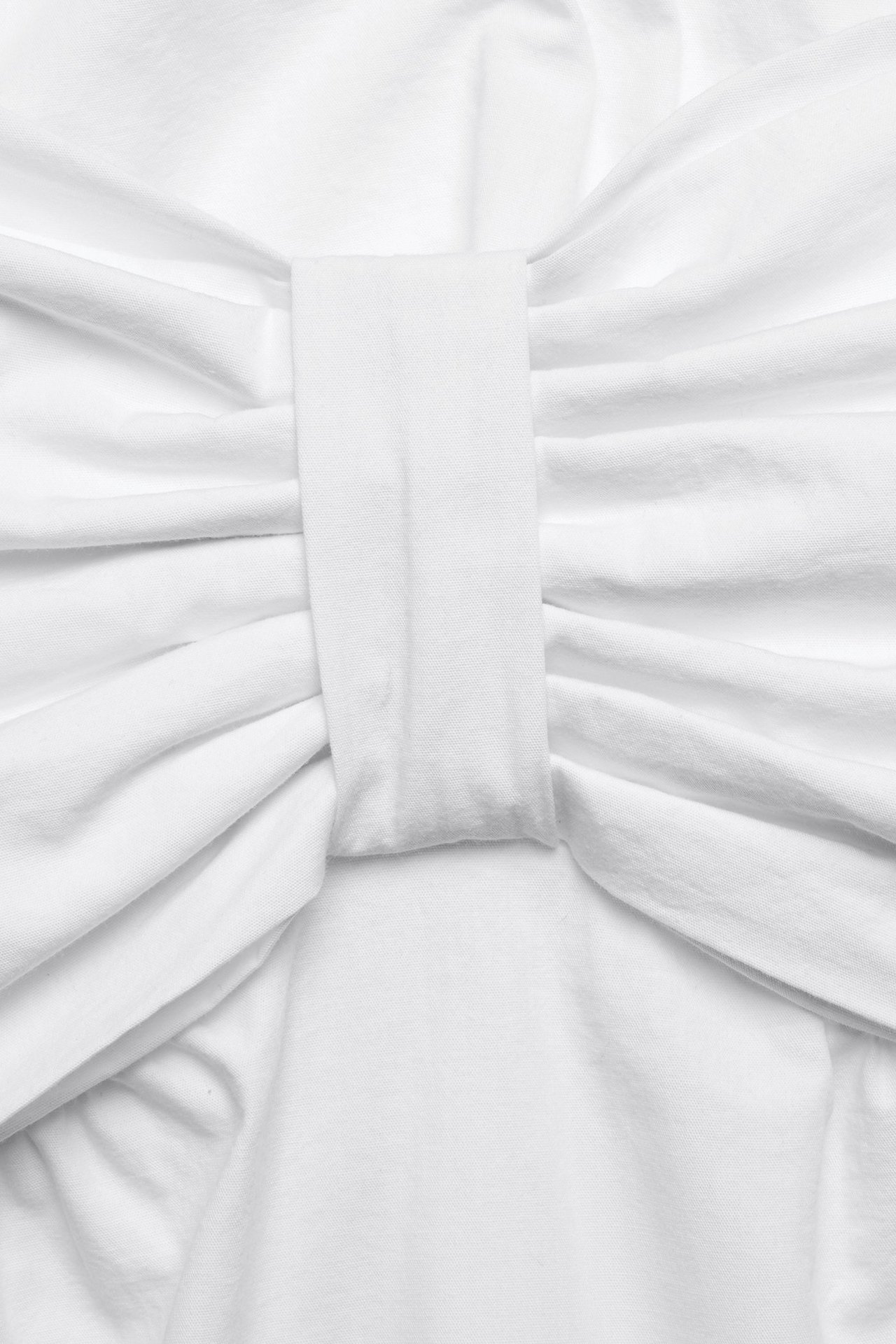 Zbliżenie białego bawełnianego topu z marszczonym, kokardkowym detalem z przodu.