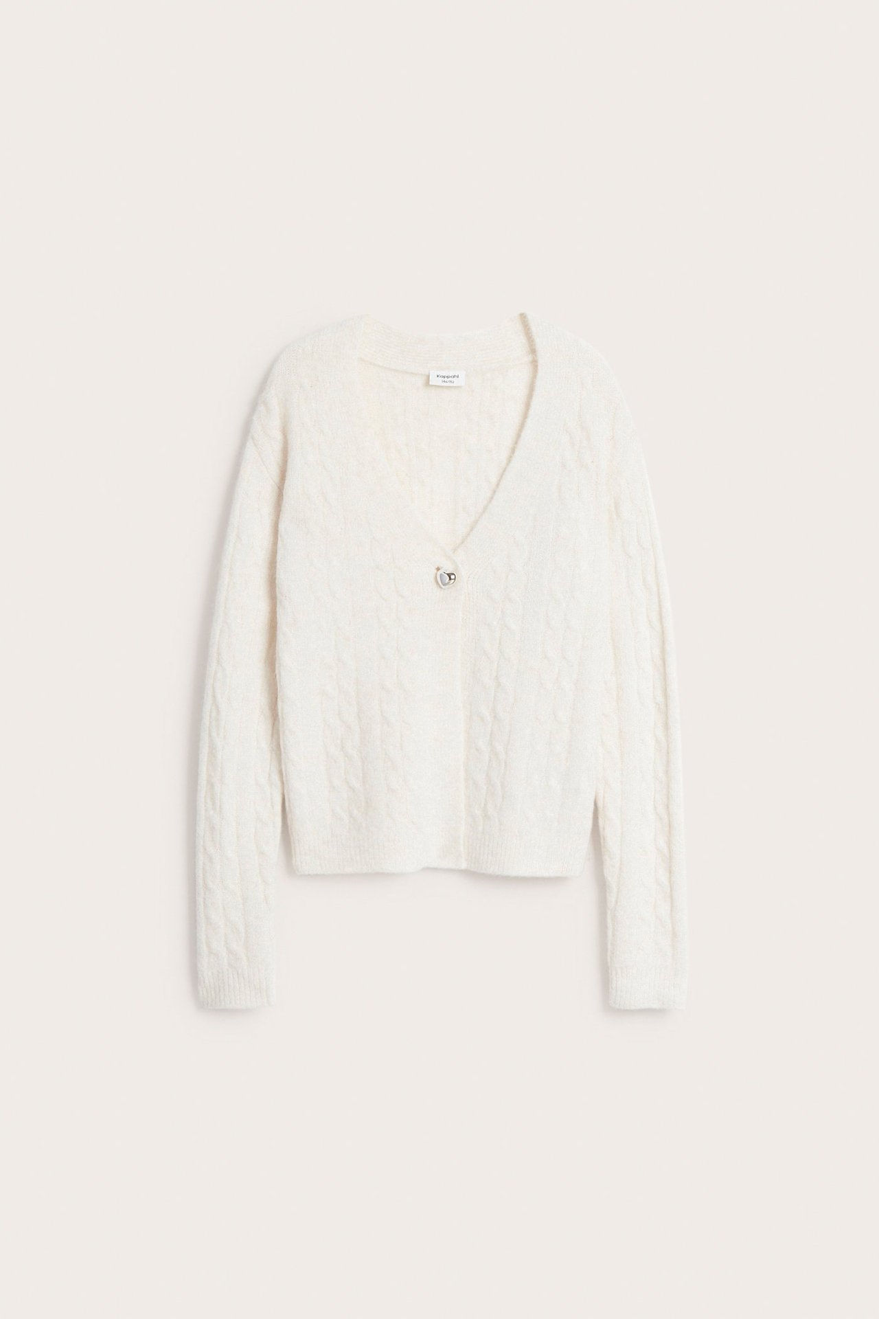 Framifrån, vit kabelstickad kofta med en hjärtformad metallknapp.