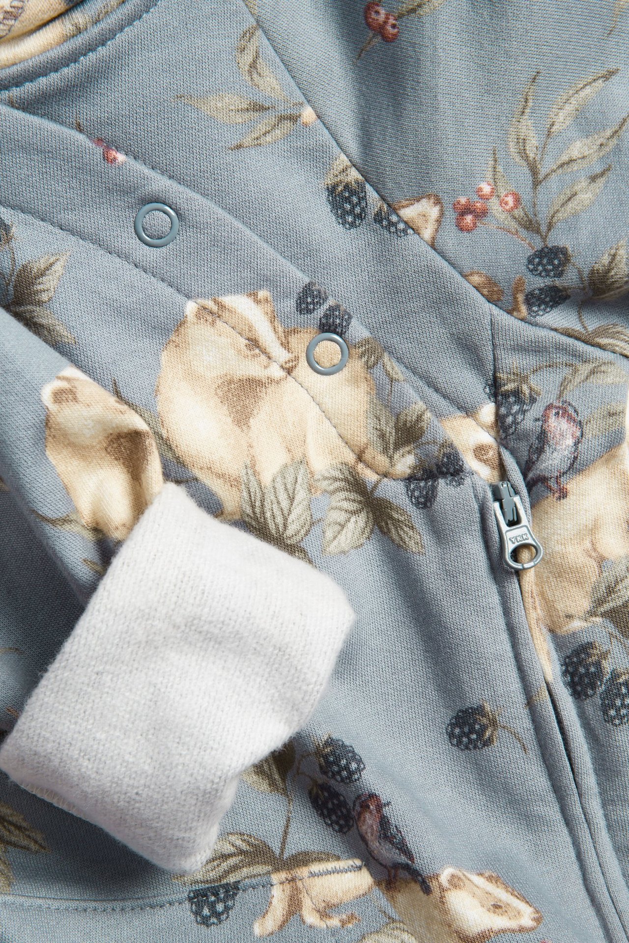 Zbliżenie na jasnoniebieski bawełniany kombinezon niemowlęcy z nadrukiem zwierzęcym, zatrzaskami i zamkiem.