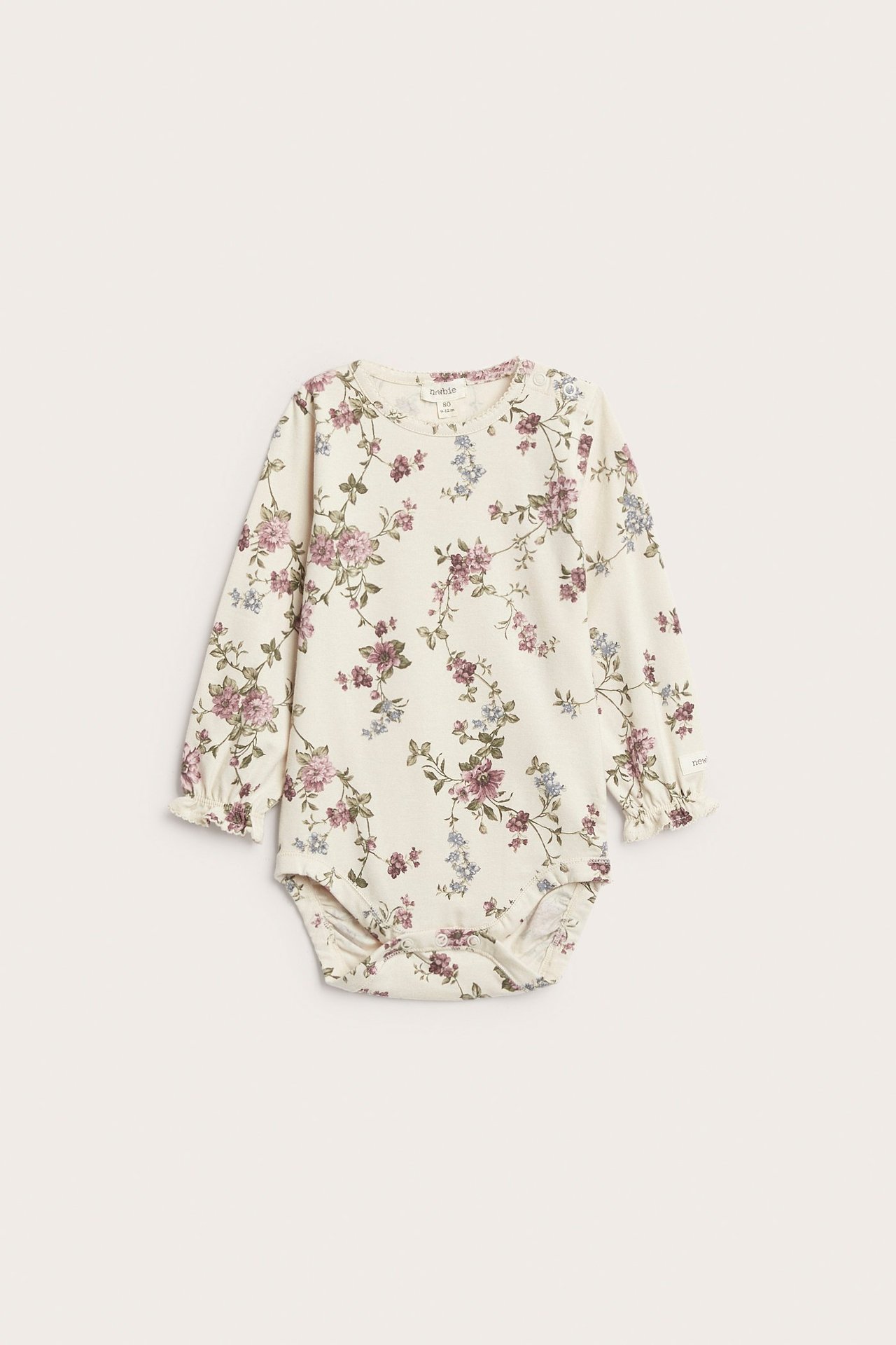 Edestä kuvattu vaalea beige vauvan body kukkakuviolla, pussihihoilla, röyhelöillä ja neppareilla.