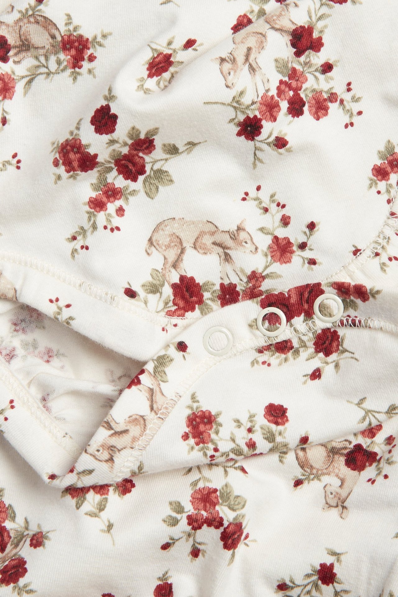 Zbliżenie na ecru body niemowlęce w kwiaty i sarny, zapinane na zatrzaski.
