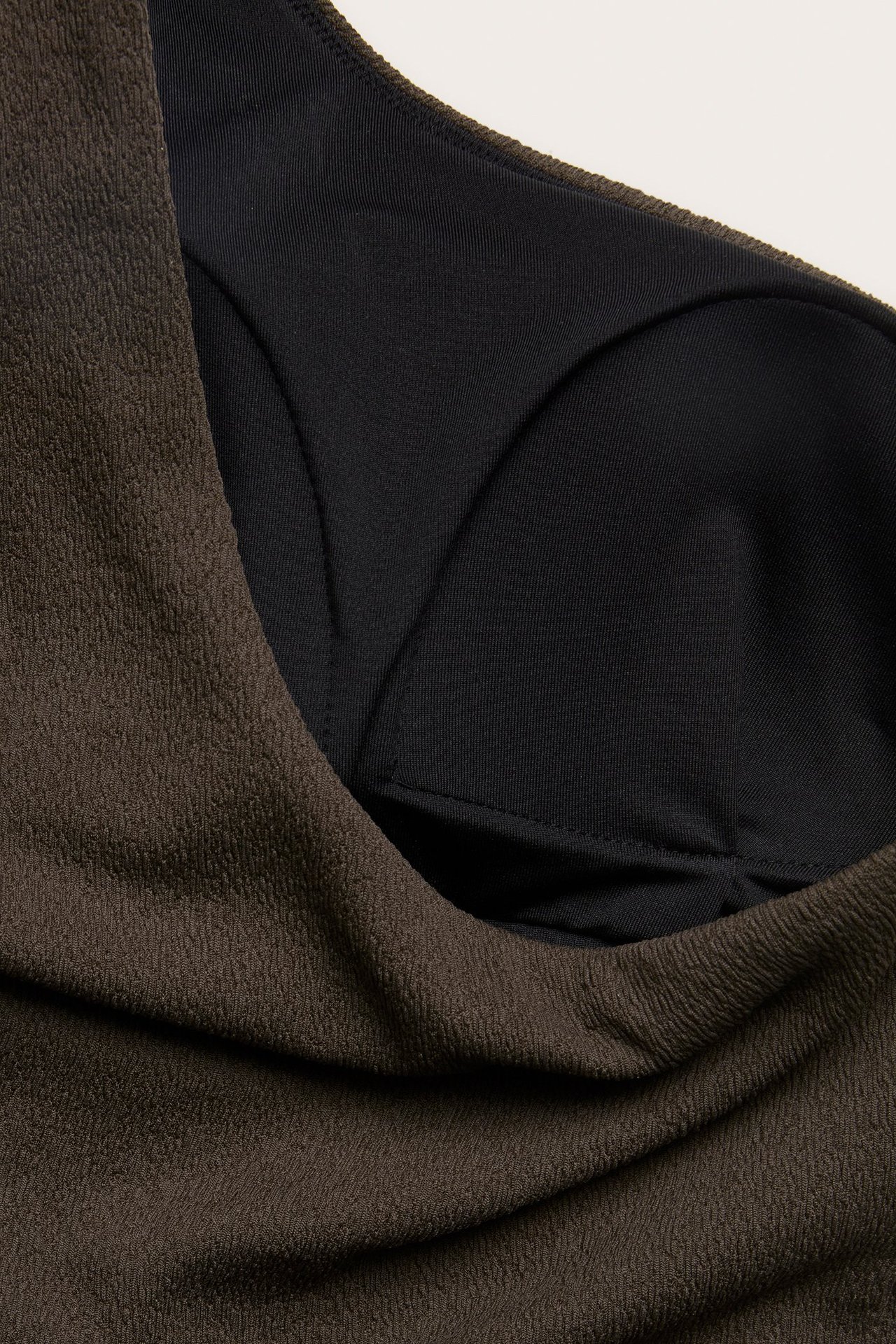 Zbliżenie brązowego, teksturowanego jednoramiennego kostiumu kąpielowego z czarną podszewką i usztywnianą miseczką.