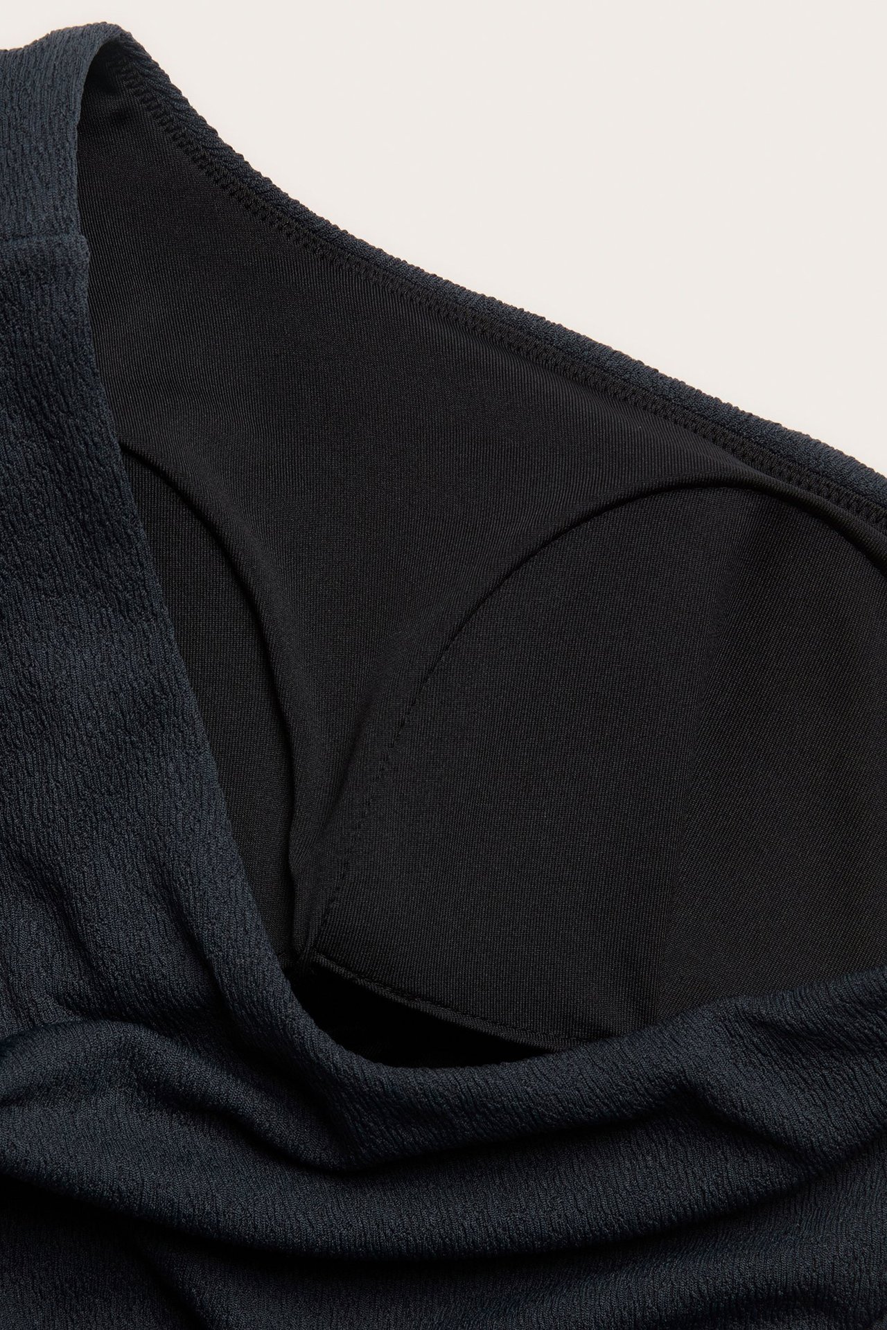 Zbliżenie na granatowy jednoramienny strój kąpielowy z teksturowanej tkaniny z widocznymi wyściełanymi miseczkami.