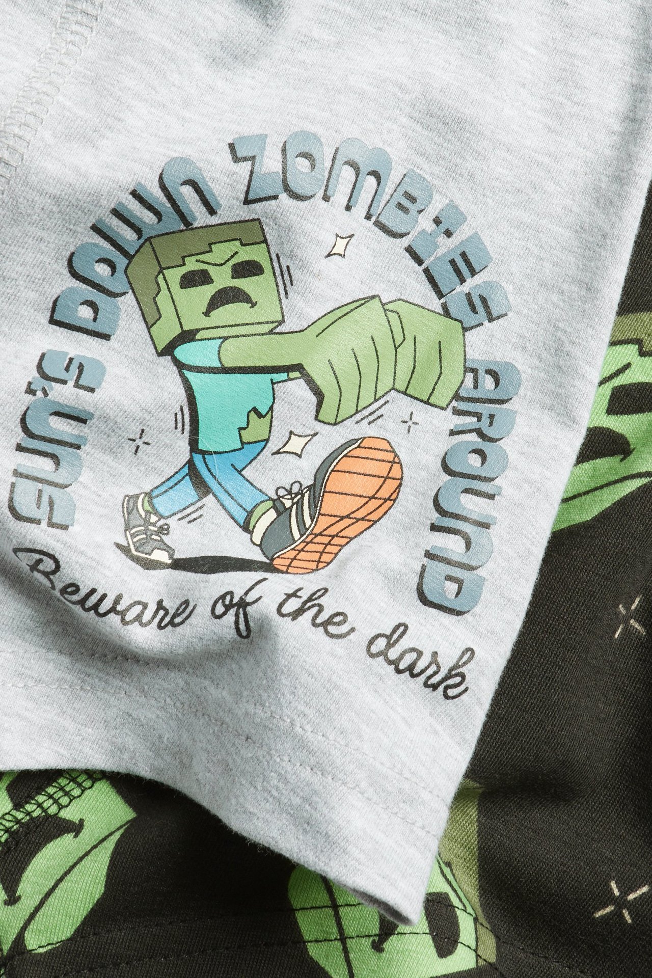 Zbliżenie na jasnoszare bokserki dziecięce z nadrukiem zombie Minecraft, obok ciemnozielonych wzorzystych bokserek.