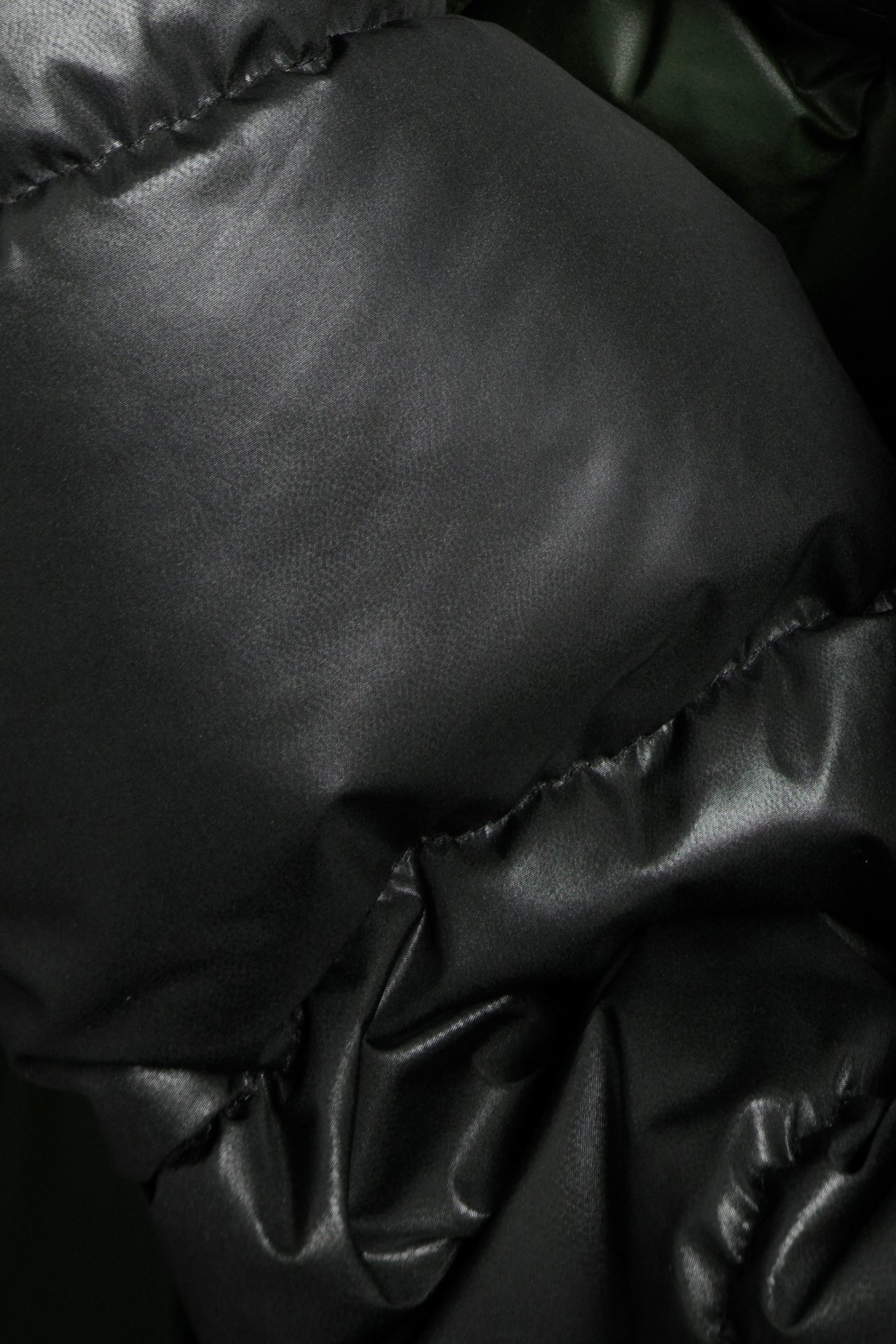 Zbliżenie czarnej, półbłyszczącej kurtki puchowej z recyklingowanego poliestru.