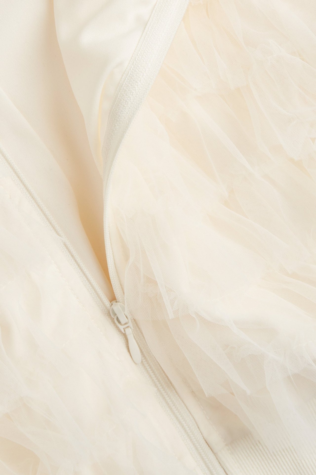 Zbliżenie na kurtkę domową w kolorze ecru z falbanami z siateczki i zamkiem.