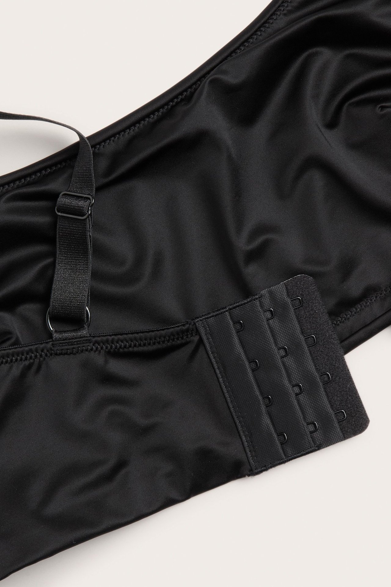 Zbliżenie czarnego, nieusztywnianego biustonosza z mikrosatyny z regulowanym ramiączkiem i zapięciem na haftki.