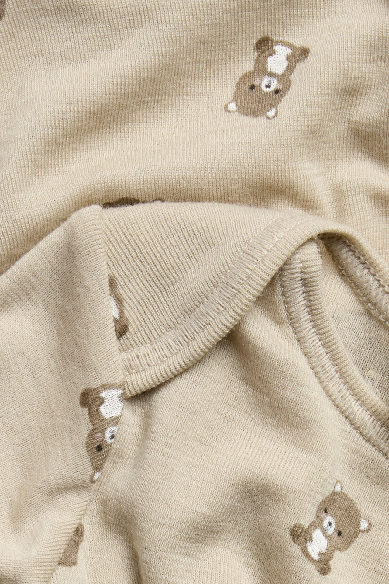 Nærbilde av en beige babybody i merinoull med brunt bjørnemønster.