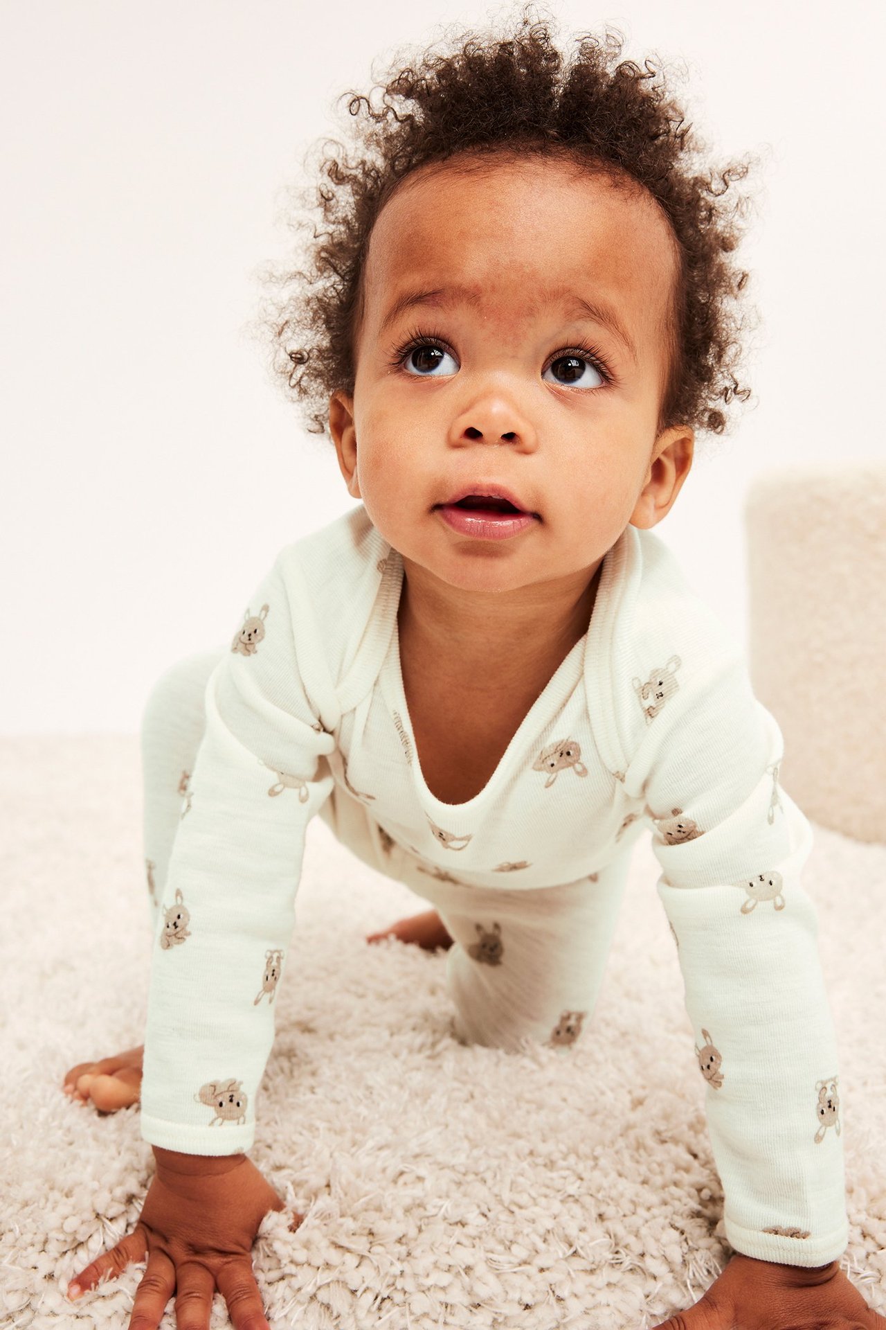 Frontvisning av en krabbende baby i lys beige merinoullbody med kaninmønster og matchende leggings.
