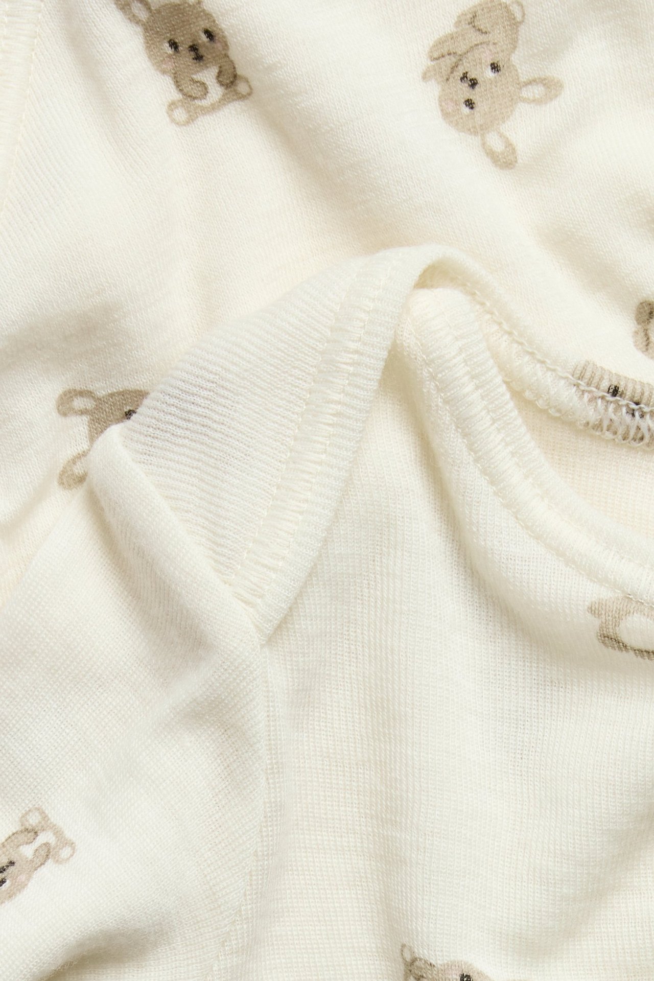 Zbliżenie na jasnobeżowe body niemowlęce z wełny merynosów z brązowym wzorem królików.