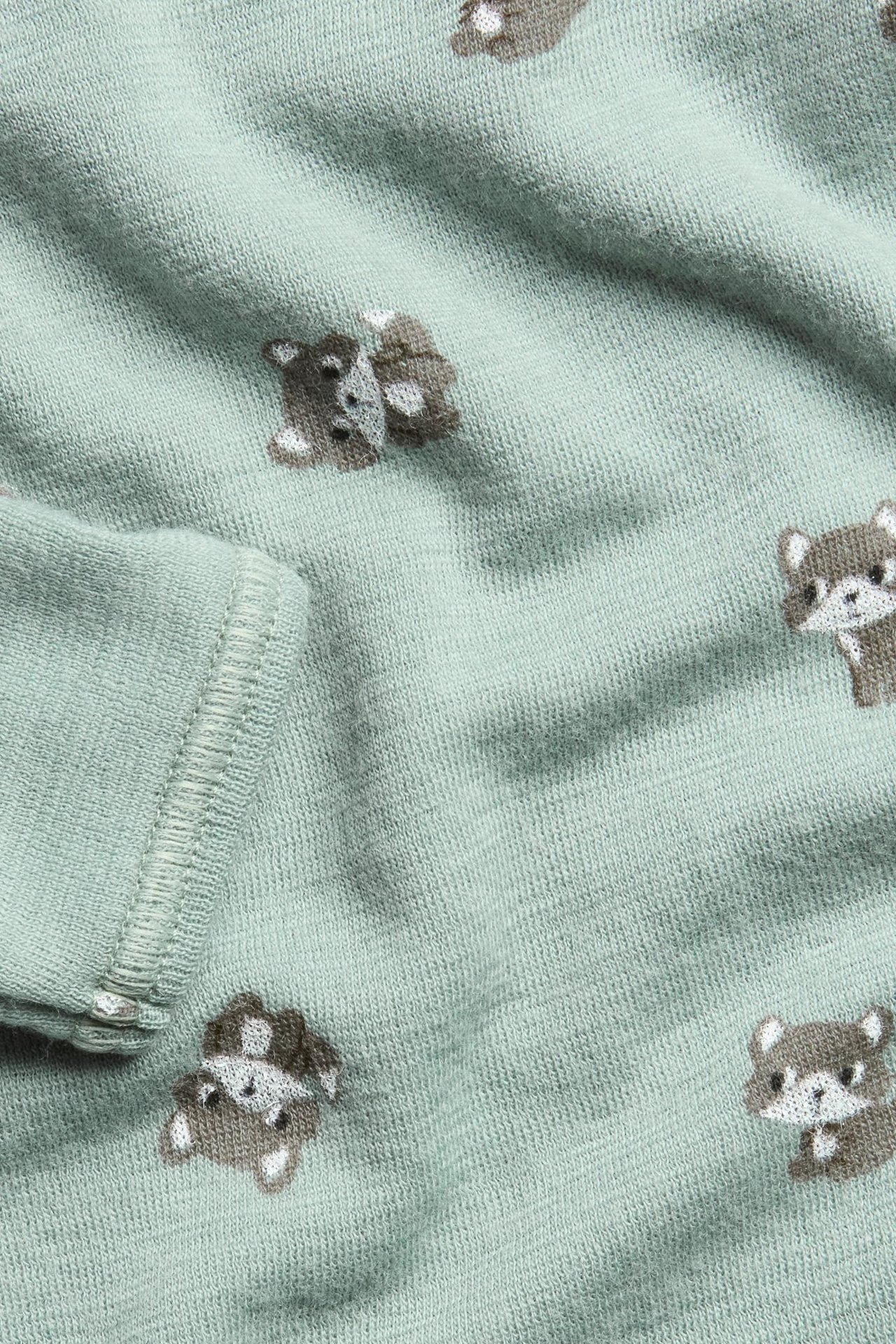 Zbliżenie jasnozielonego body niemowlęcego z wełny merynosów w brązowy wzór lisów.