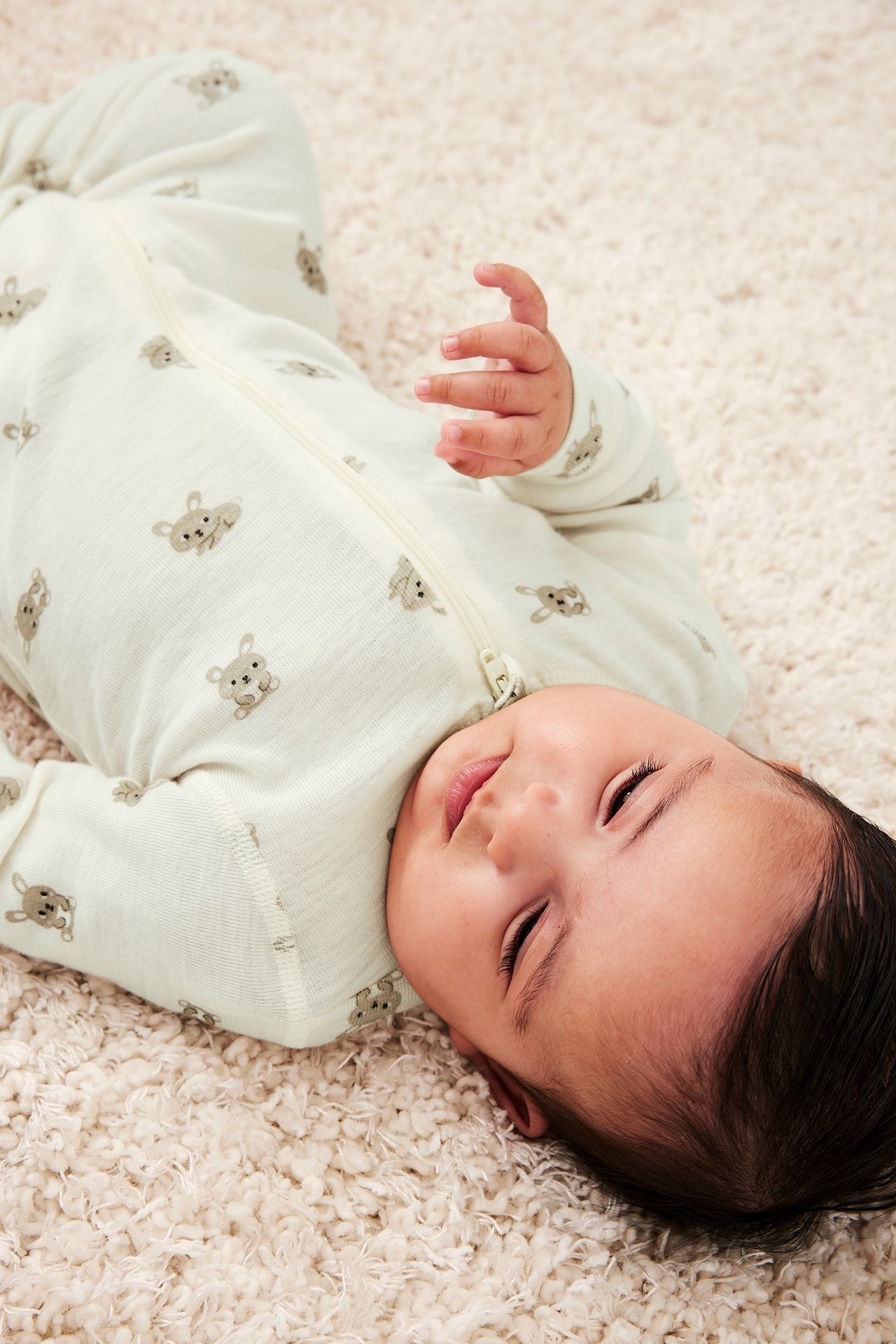 Nærbilde av baby som har på seg en lys beige merinoull sparkebukse med kaninmønster og glidelås.