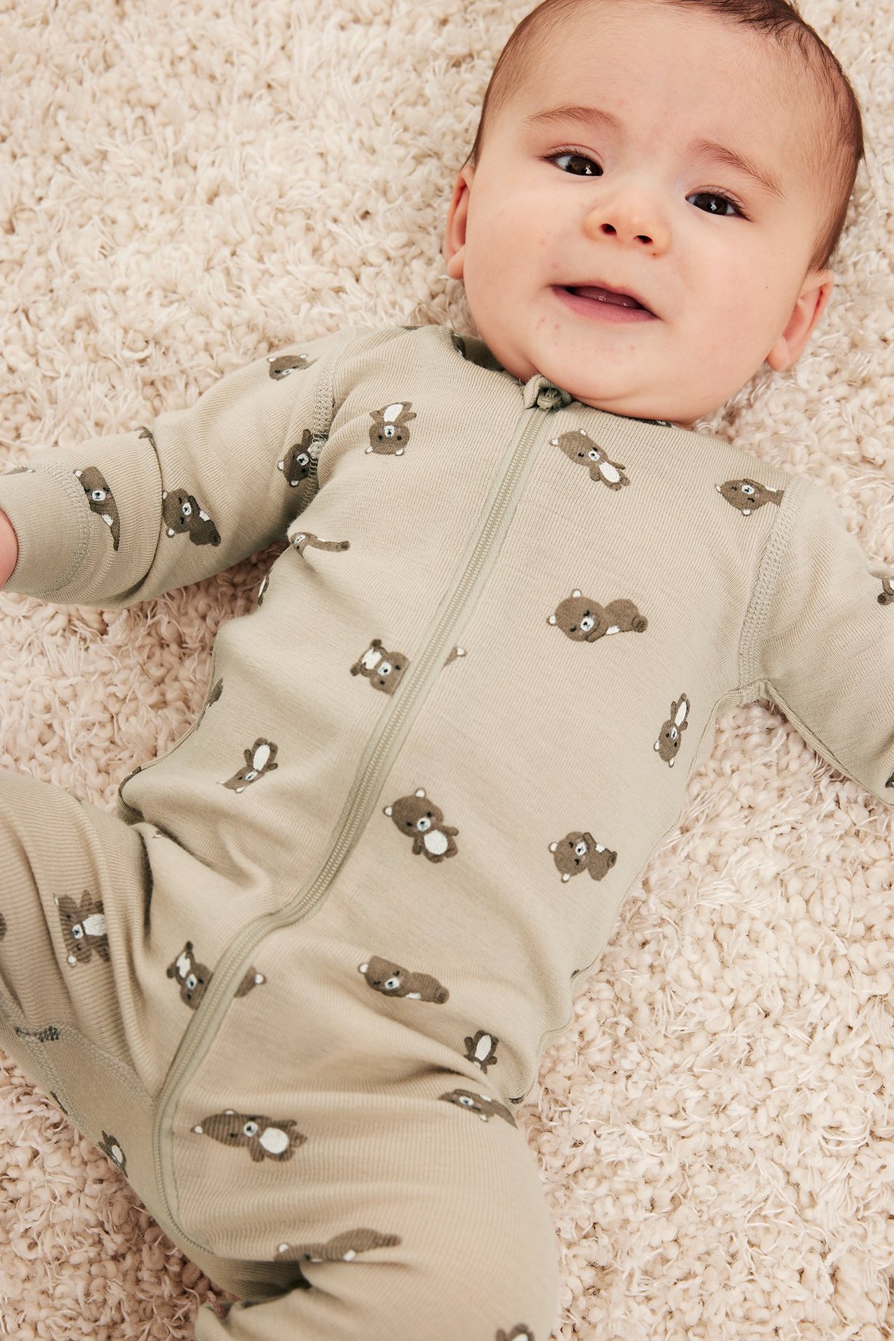 Ovenfra: Baby i beige merinoull-sparkedress med brunt bjørnemønster, glidelås foran.