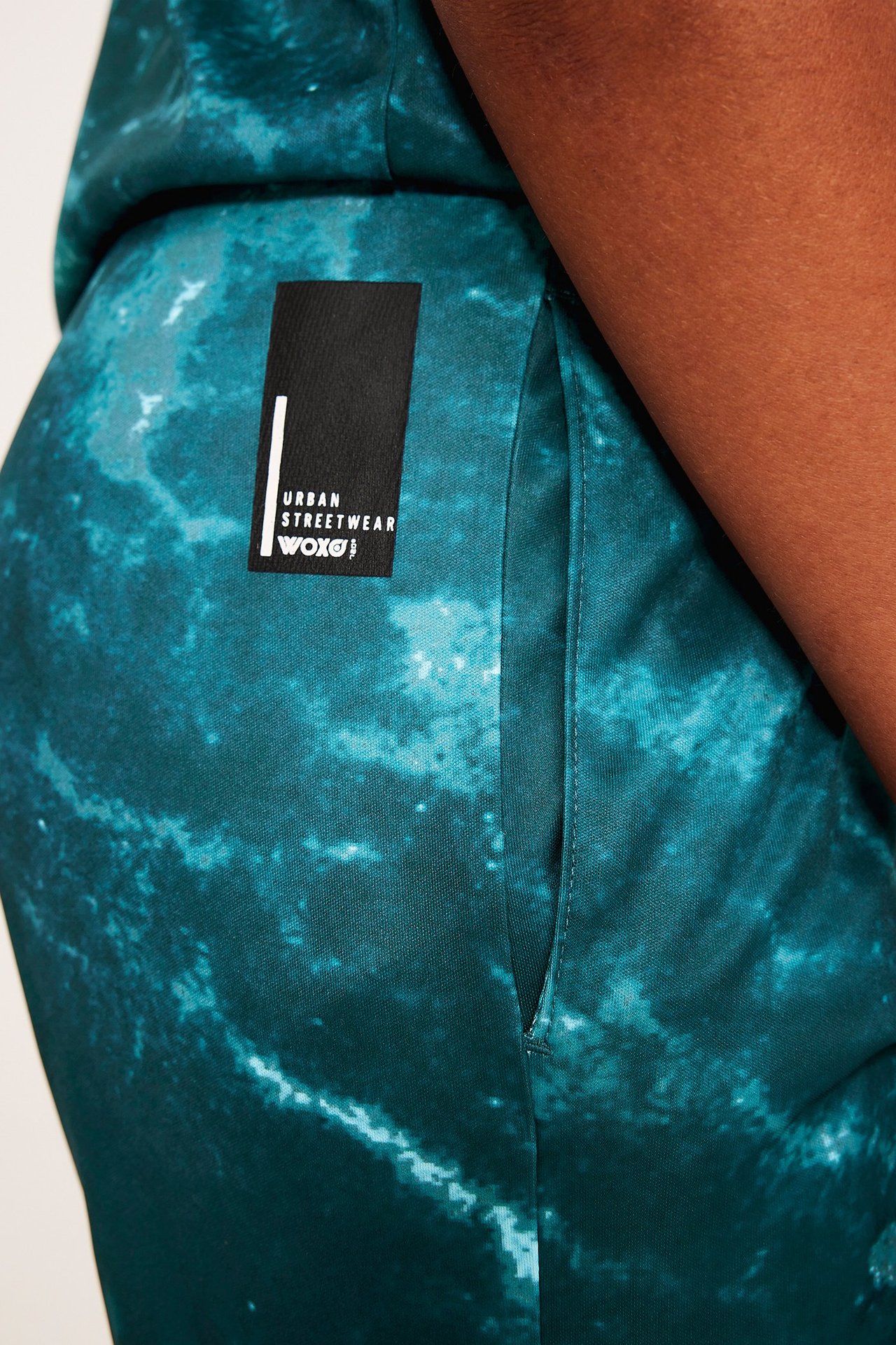 Zbliżenie na zielone, wzorzyste szorty dziecięce z poliestru z boczną kieszenią i czarną metką 'WOXO'.