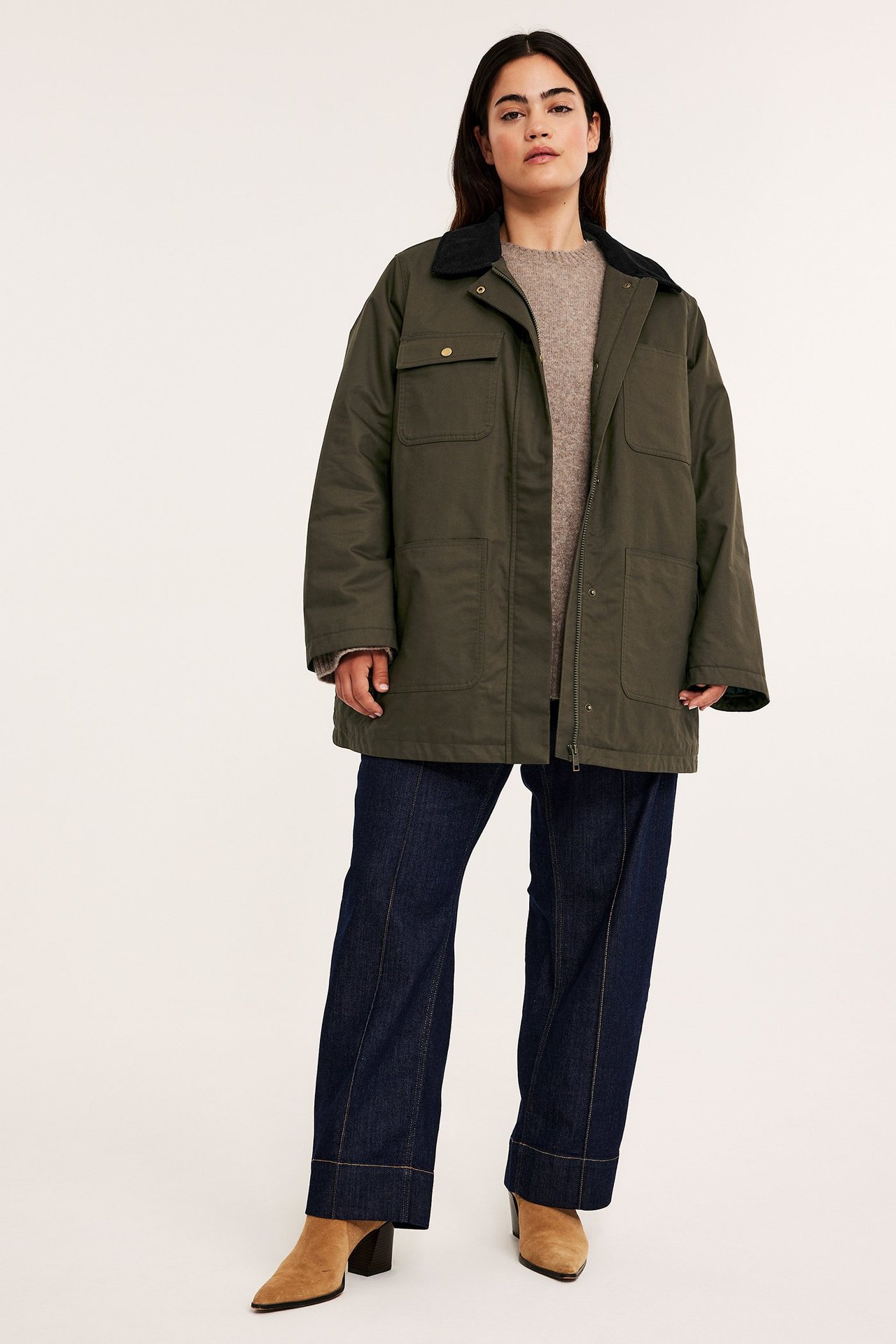 Framifrån: kvinna i khaki canvasjacka med svart manchesterkrage, mörkblå jeans, beiga ankelstövlar.