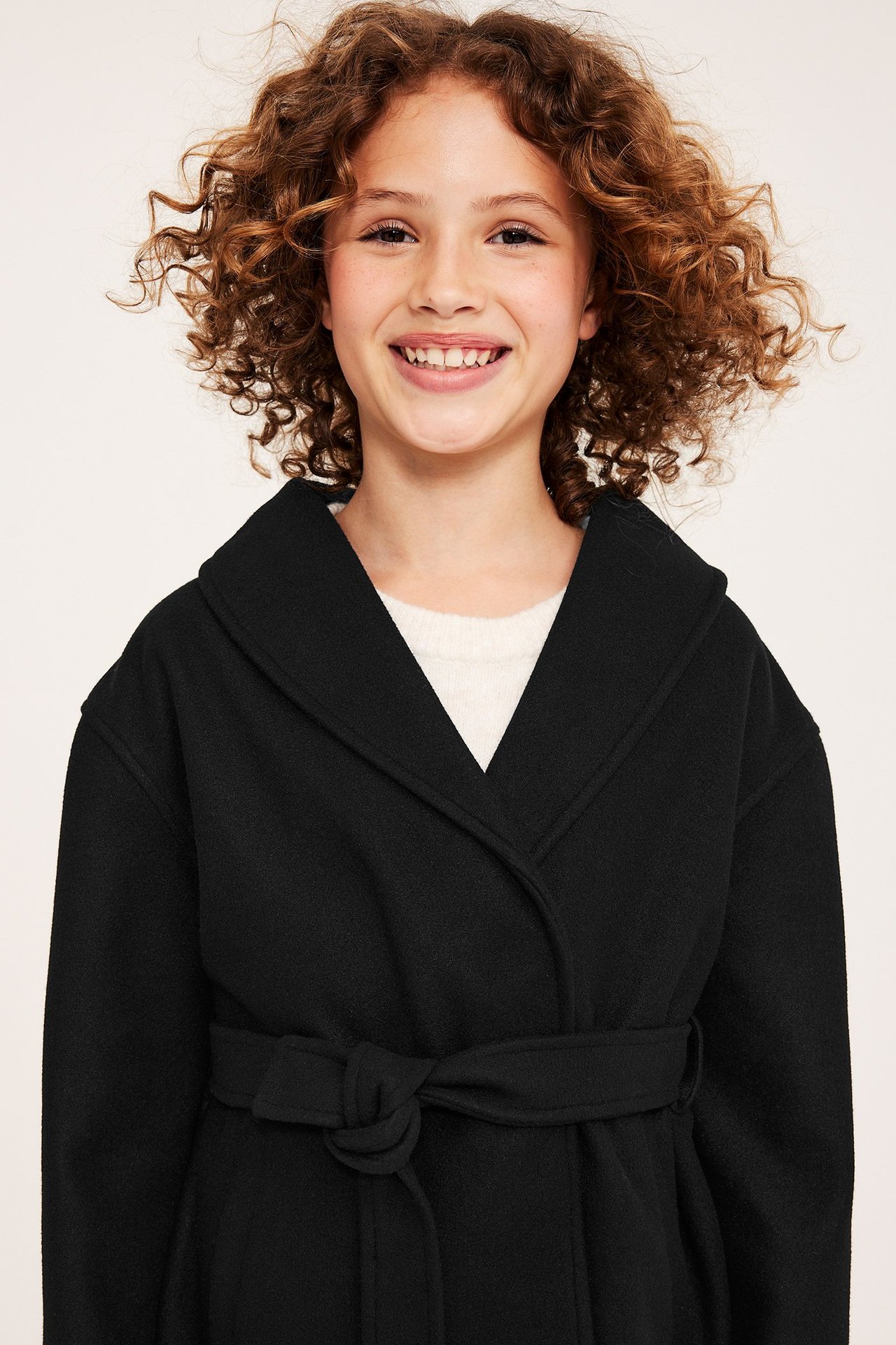Framifrån, leende barn i svart polyesterjacka med knytskärp över en ljus tröja.