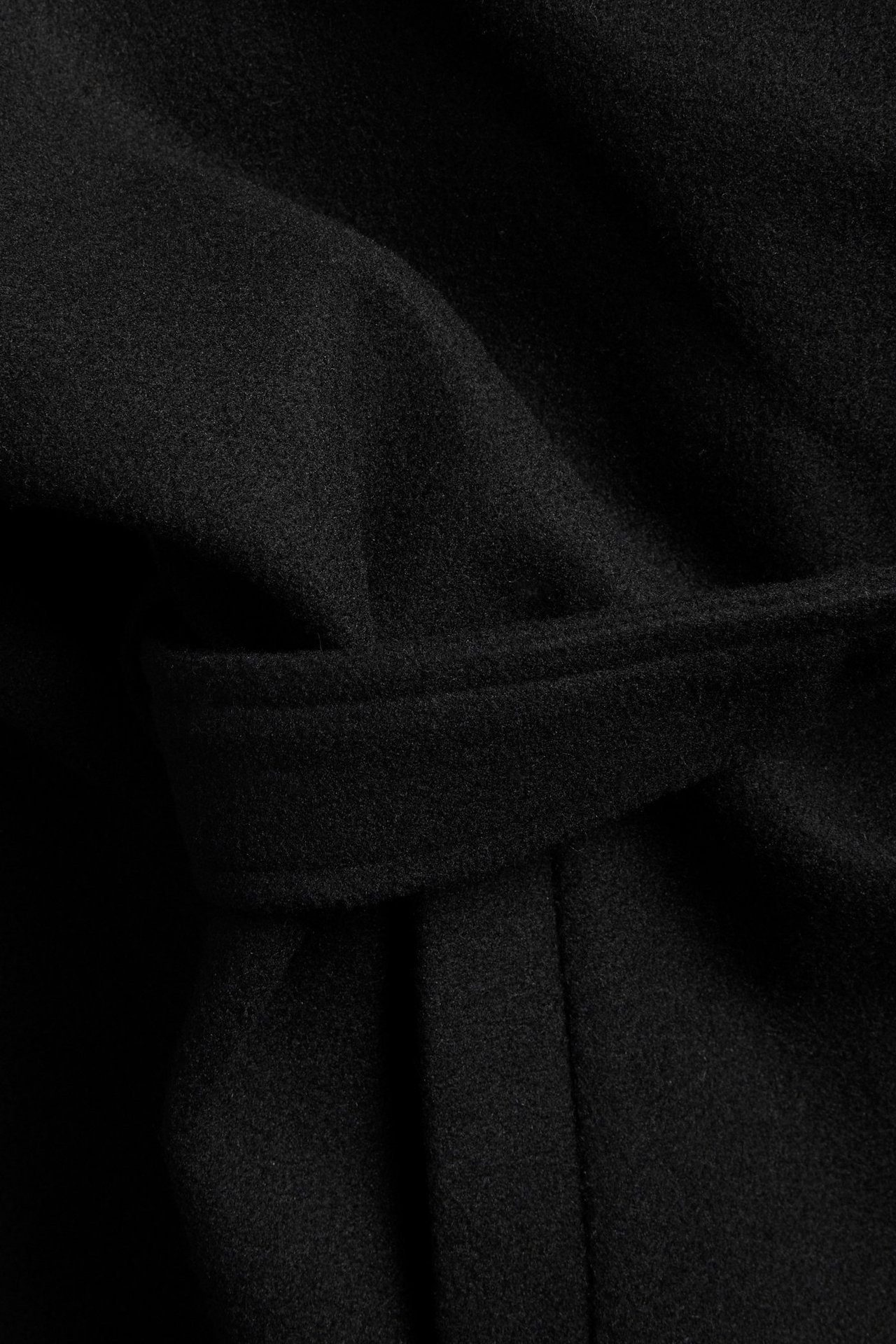 Zbliżenie czarnej jednolitej kurtki poliestrowej z wiązanym paskiem w talii.