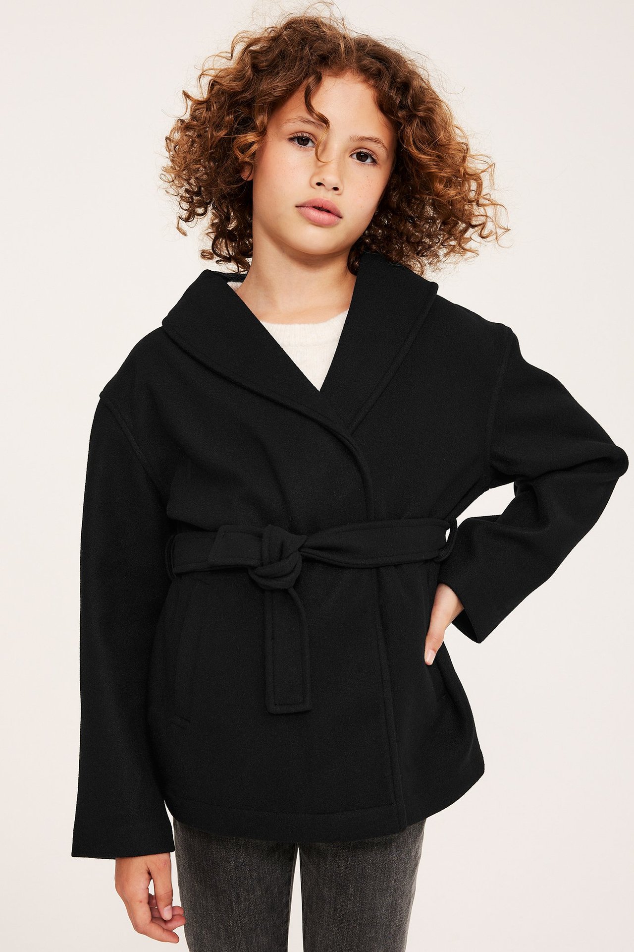 Framifrån, ett barn i svart polyesterjacka med knytskärp, över en ljus topp.