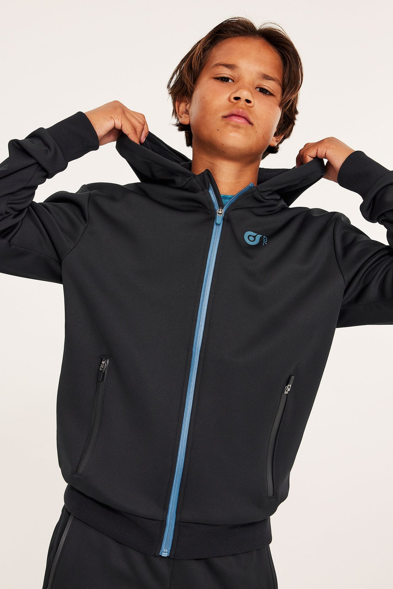 Widok z przodu: Dziecko w czarnej poliestrowej bluzie z kapturem, z niebieskim zamkiem, niebieskim nadrukiem i bocznymi kieszeniami.