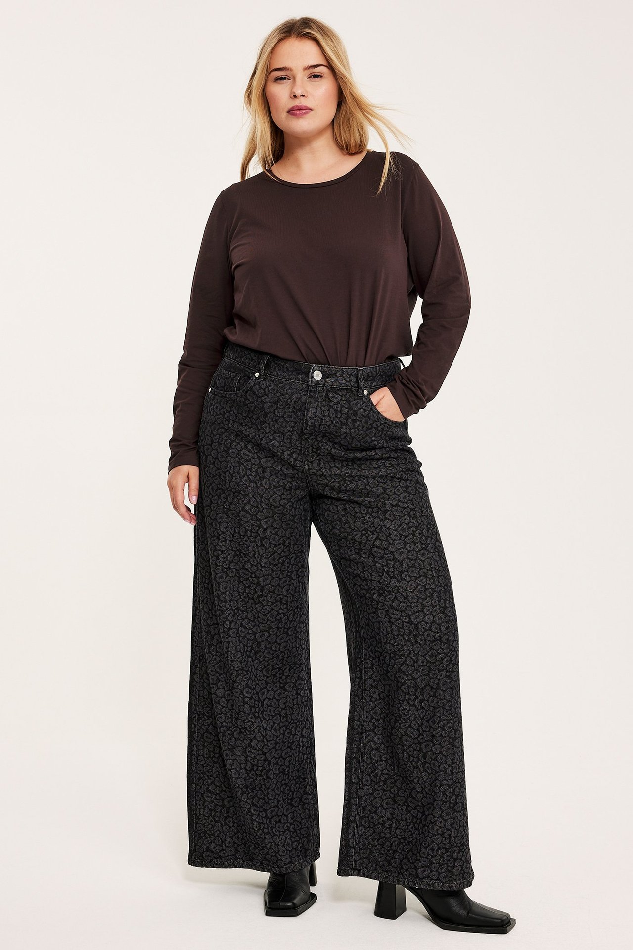 Forfra: kvinne i mørkerød langermet topp, mørkegrå mønstrede vide bukser og svarte støvler.