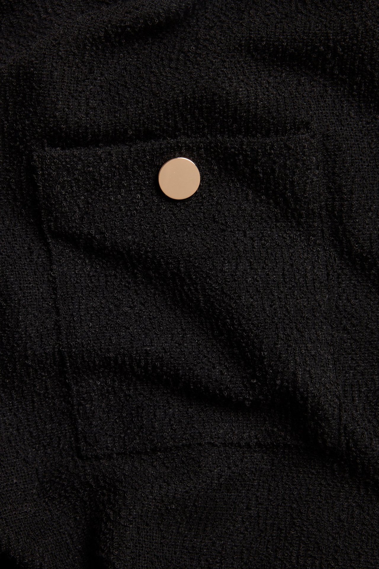 Zbliżenie czarnej sukienki dżersejowej z przednią kieszenią i złotym guzikiem.