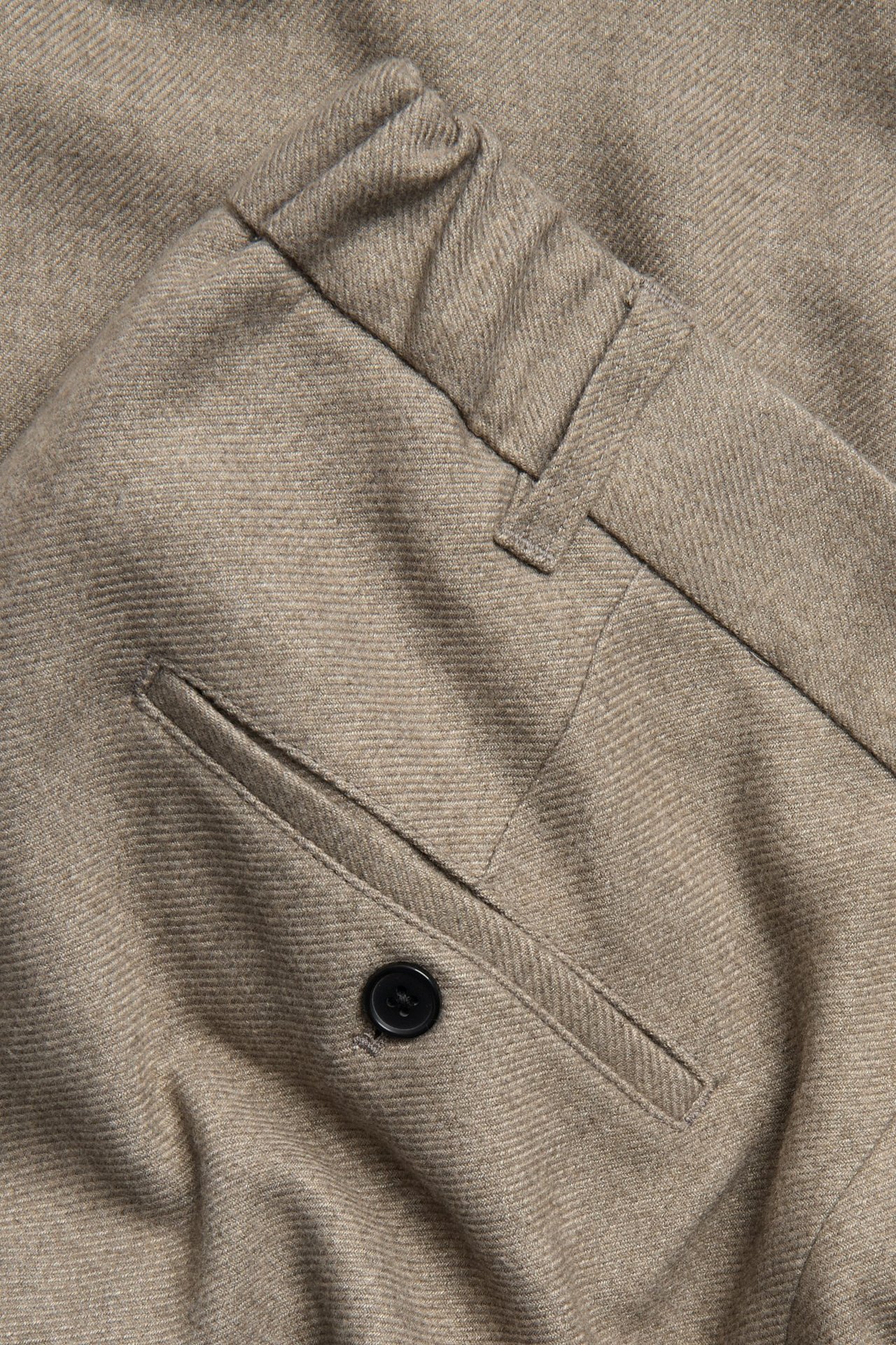 Zbliżenie na męskie beżowe melanżowe spodnie z czesanego materiału z tylną kieszenią i czarnym guzikiem.