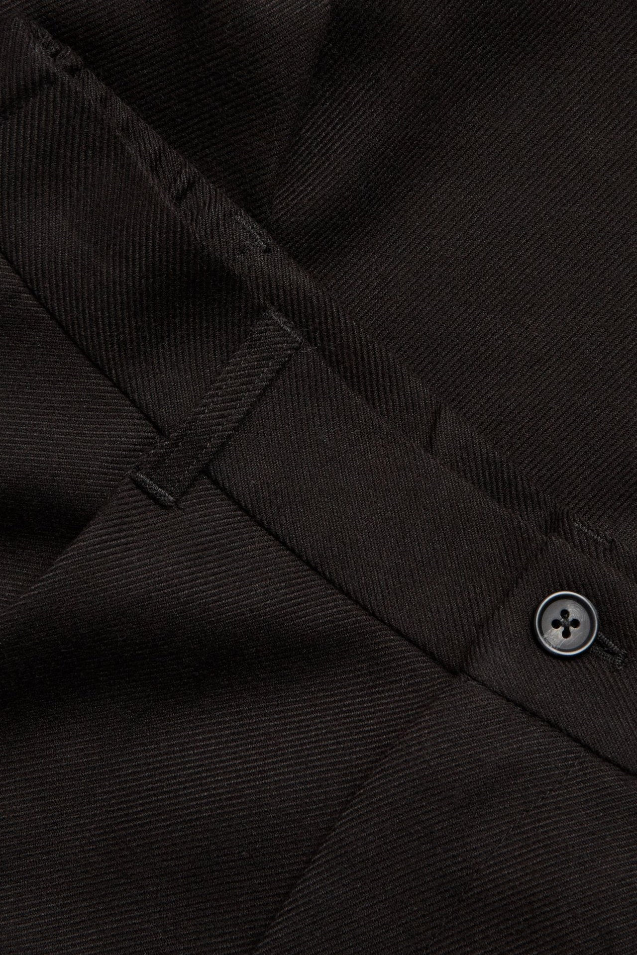 Zbliżenie na czarne szczotkowane spodnie z widocznym guzikiem i szlufką.