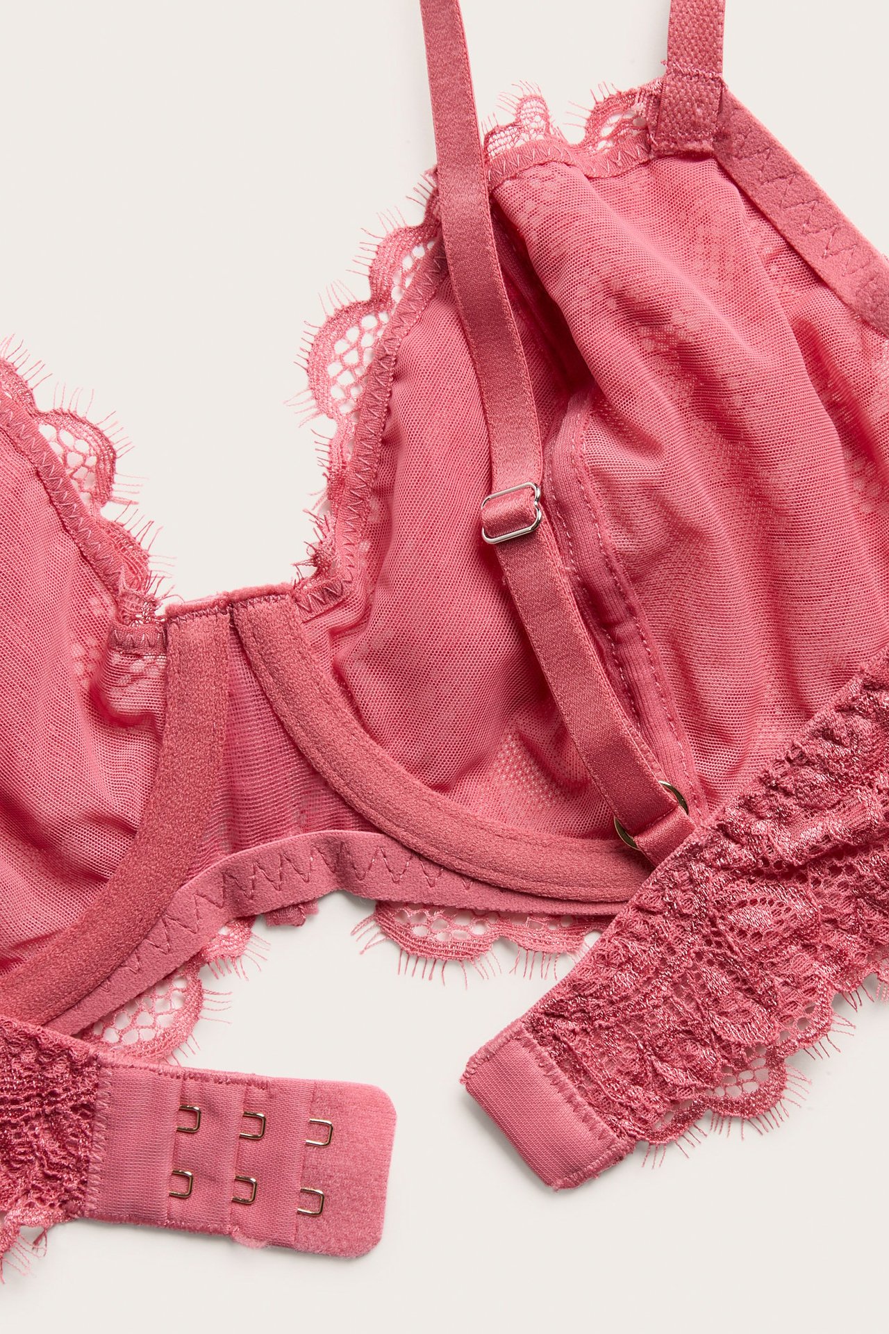 Zbliżenie z góry na koralowy, nieusztywniany biustonosz z fiszbinami, z błyszczącą koronką i zapięciem na haftki.